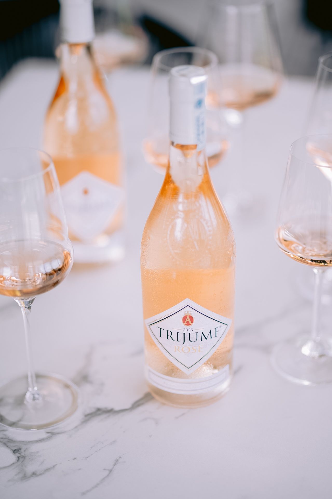 Bottle of Trijumi rose wine with wine glasses on marble surface.