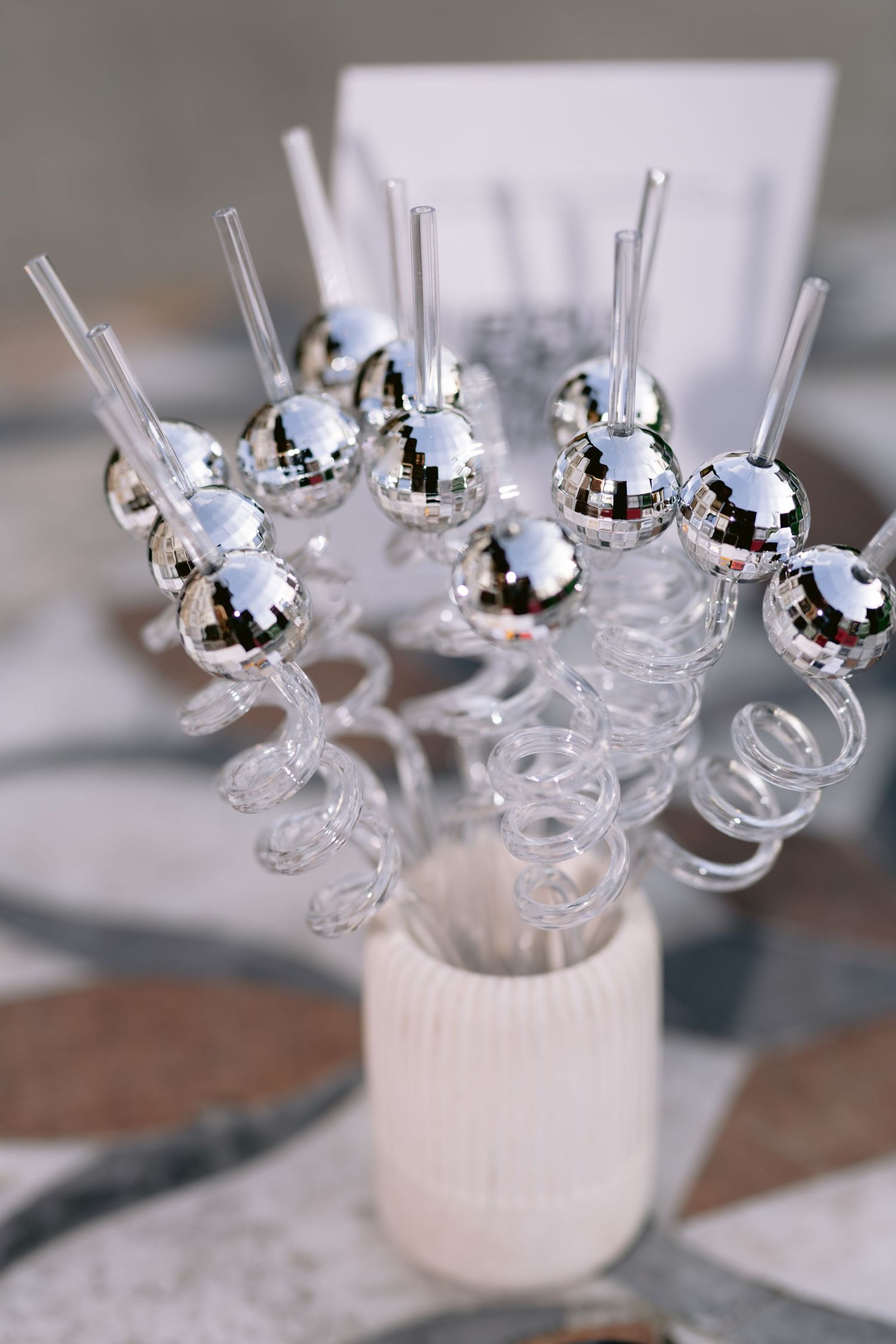 Disco ball drink stirrers with mirrored spheres and clear acrylic stems displayed in a white ceramic holder.