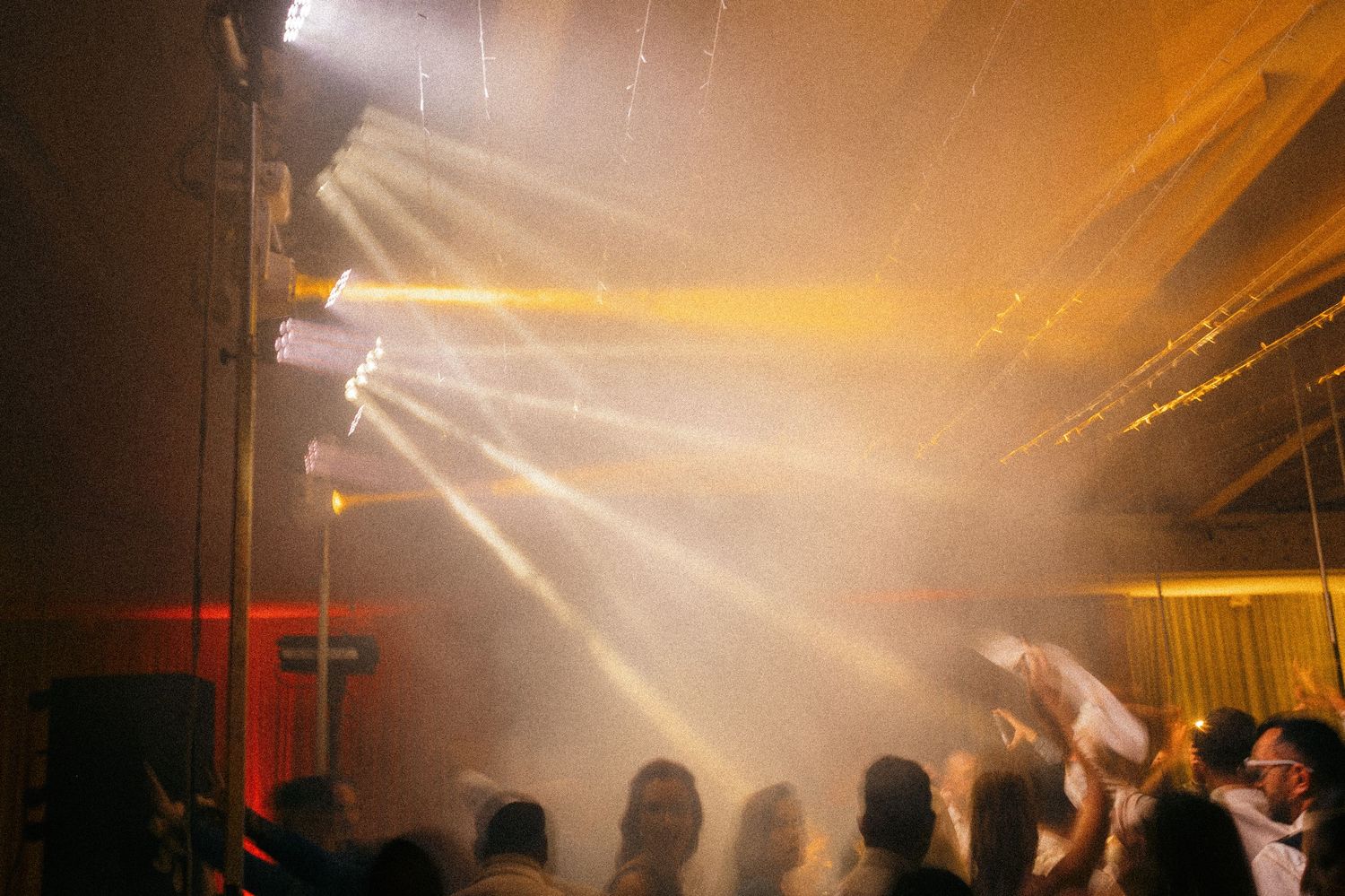 Crowd dancing under dramatic light beams and fog at an energetic nightclub party event.