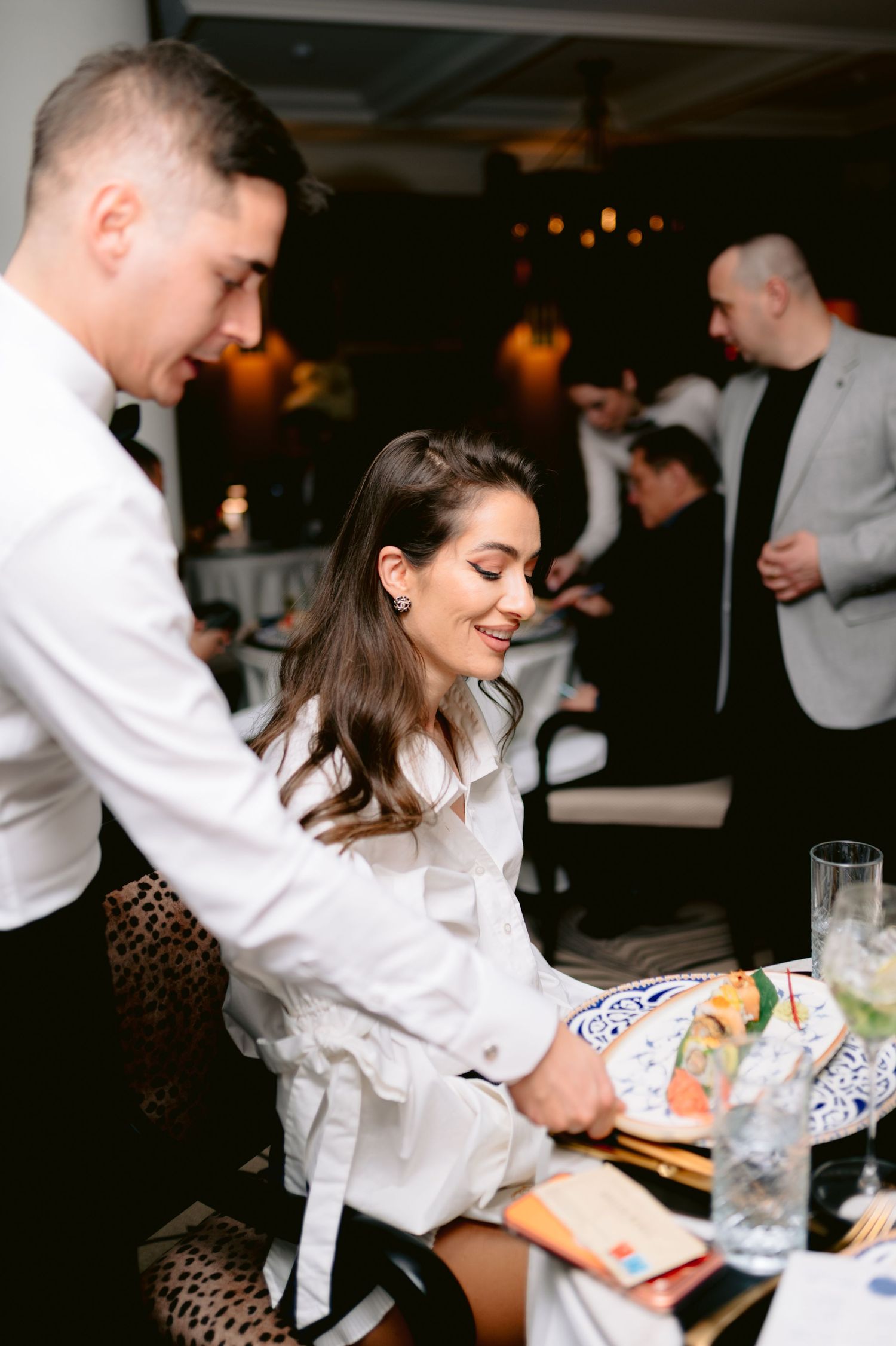 Waiter serving food to a smiling brunette woman at an elegant wedding reception dinner.