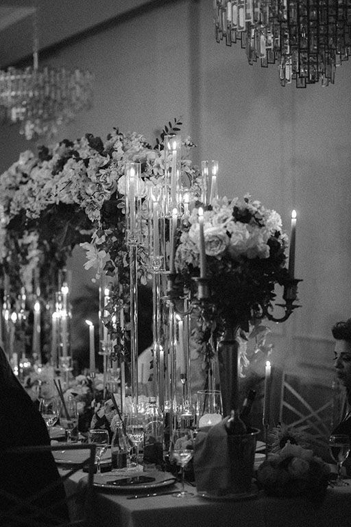Elegant wedding reception table with crystal chandeliers and tall floral centerpieces in black and white.