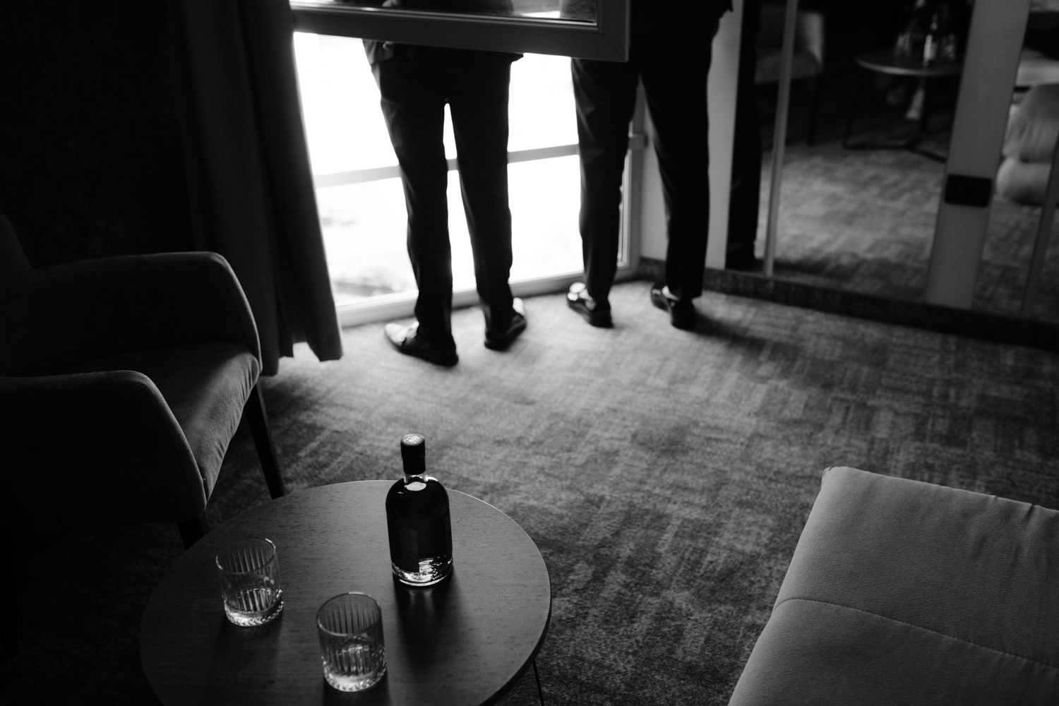 People in formal attire gathered at a dimly lit indoor event space with tables and drinks.