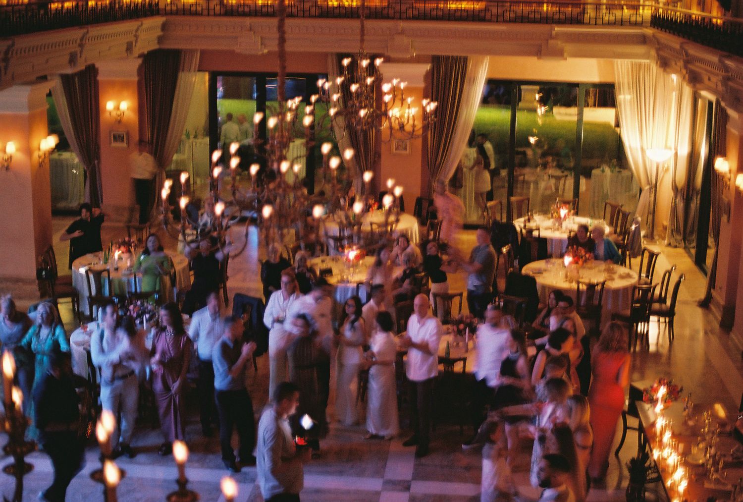 Wedding reception guests dancing and celebrating on a dimly lit dance floor with warm ambient lighting and decorations.