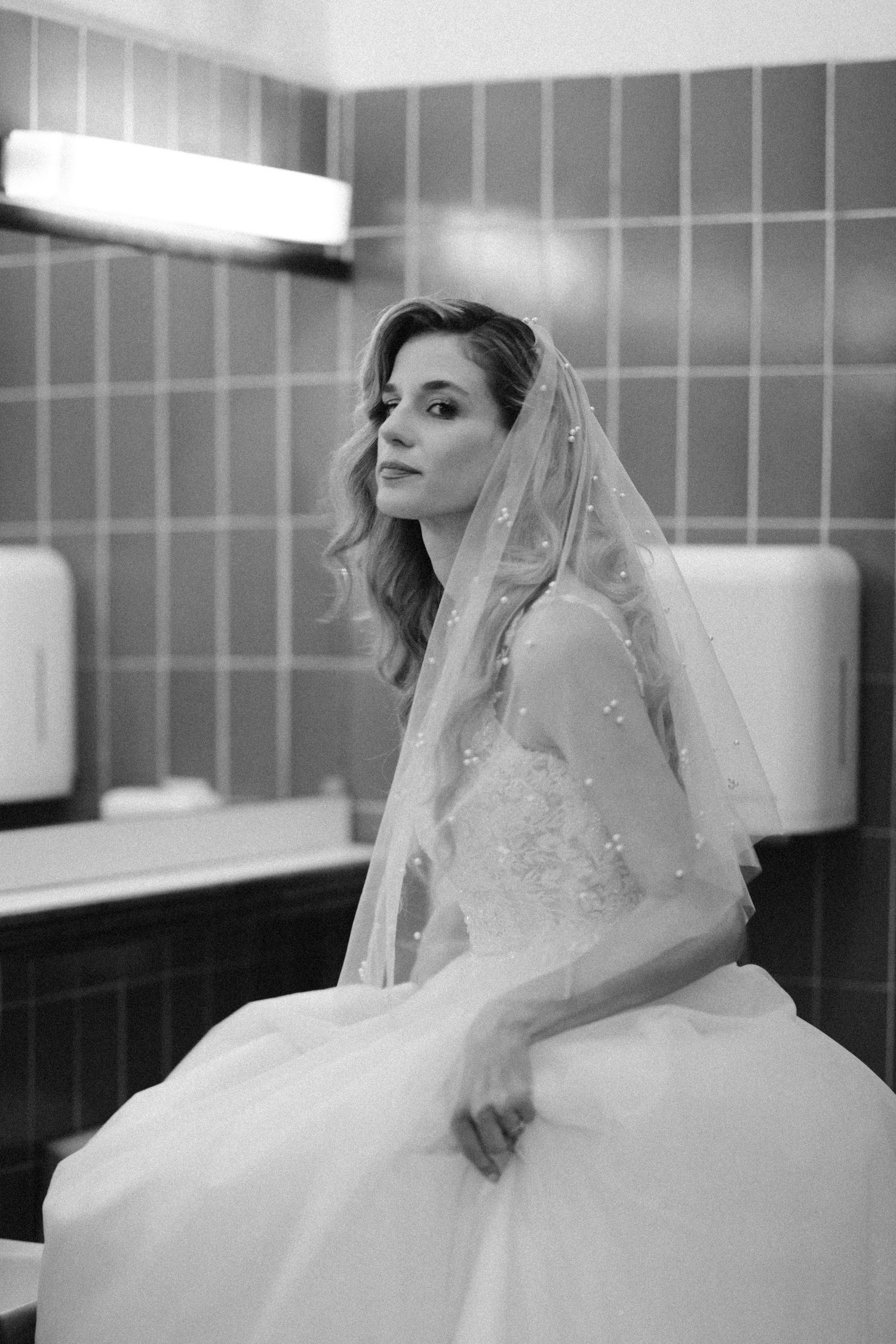 A bride in a flowing white wedding gown and veil poses elegantly in an interior setting.