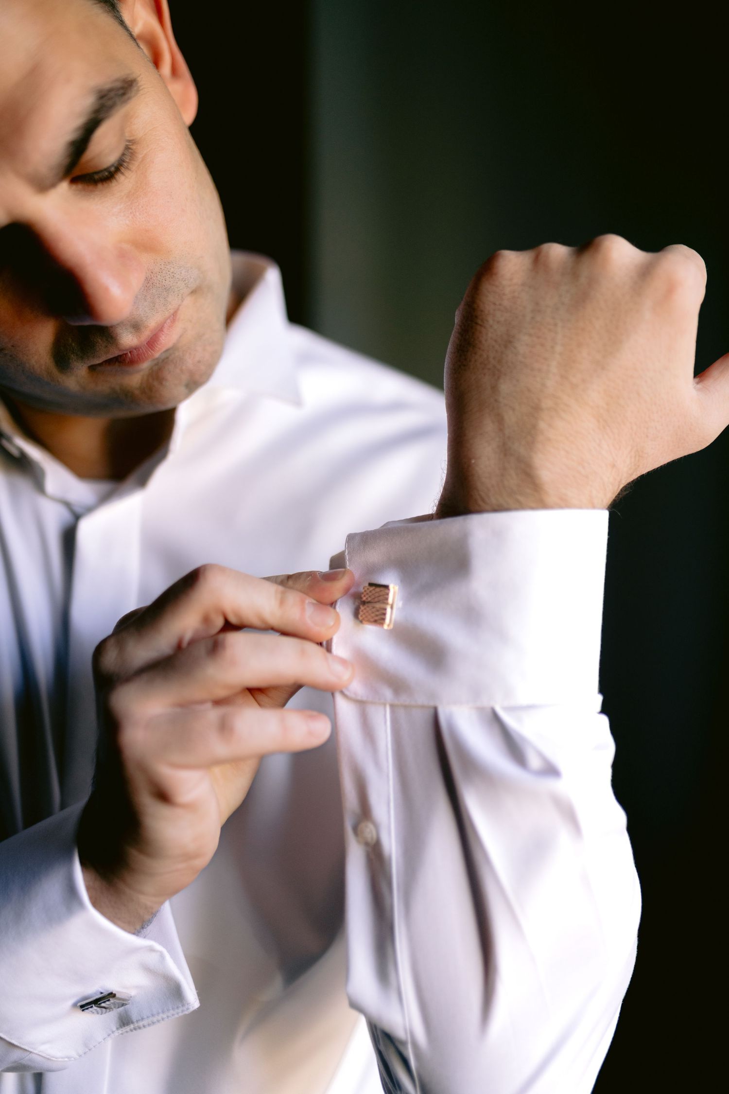 Close-up shots of a groom adjusting his white dress shirt cuff links during wedding preparations.