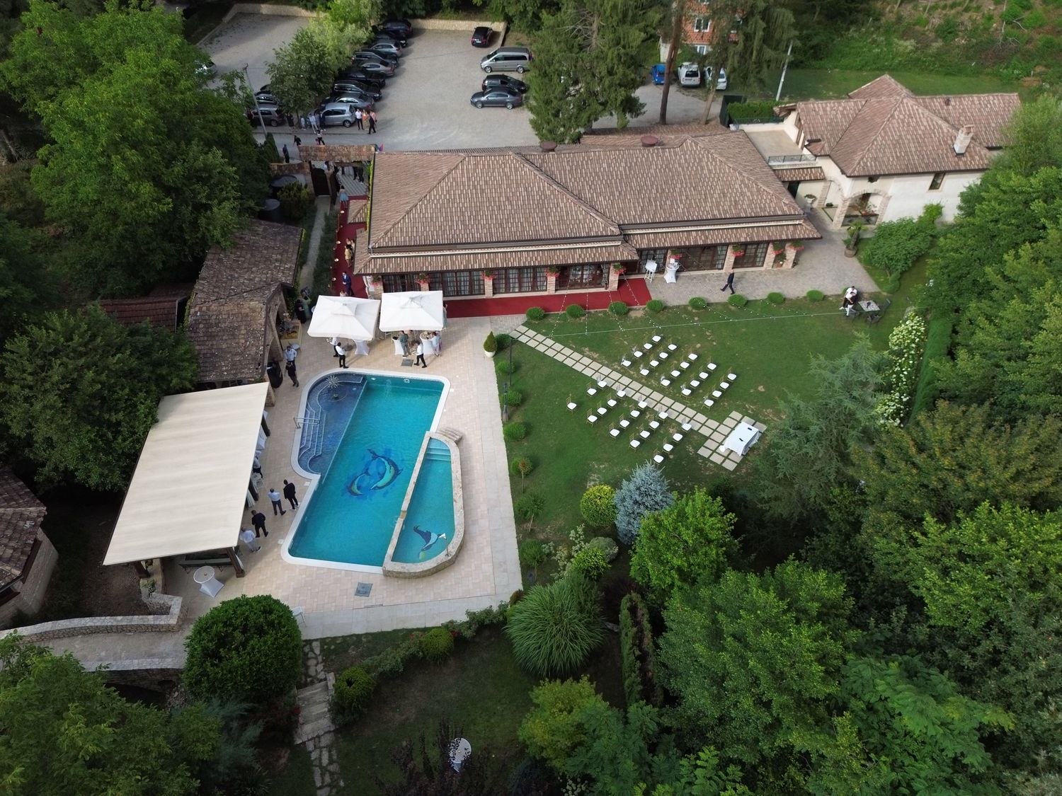 Aerial view of a luxury hotel with a swimming pool, manicured gardens, and terrace surrounded by lush green trees.