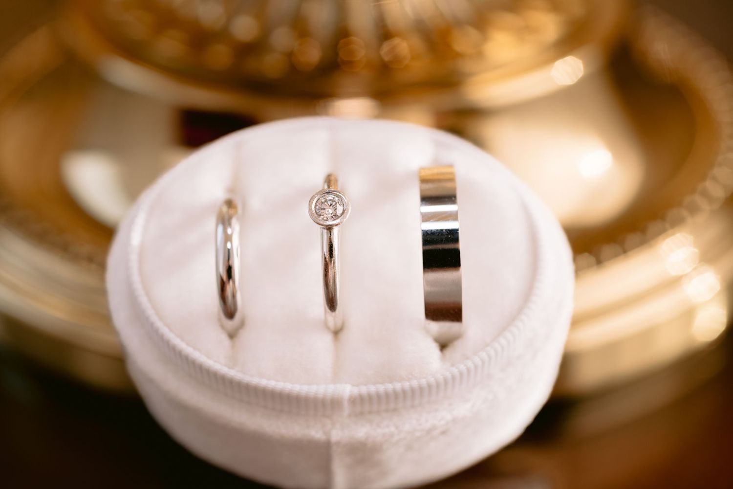 Three wedding rings displayed on a white circular ring cushion with a soft golden background glow.