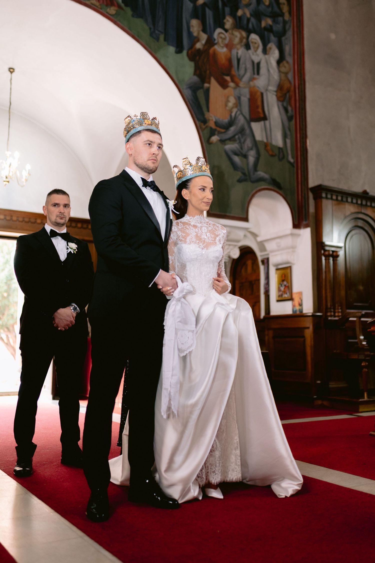 A wedding party stands in a church with red carpeting during a formal ceremony.