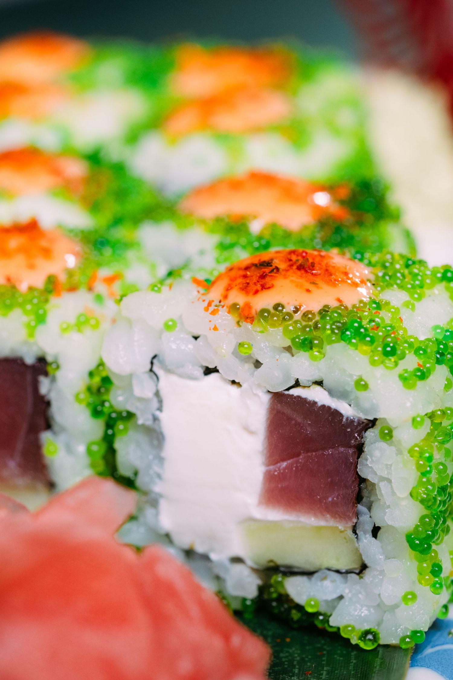Close-up of green tobiko sushi rolls filled with tuna and cream cheese, topped with spicy shrimp.
