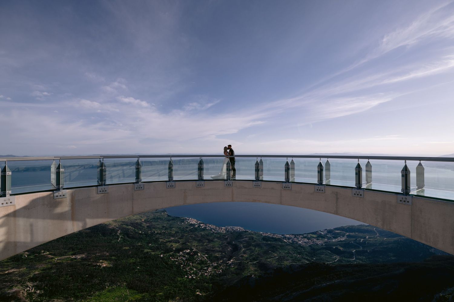 Couple embracing on a curved scenic overlook balcony with panoramic ocean and coastal landscape views.