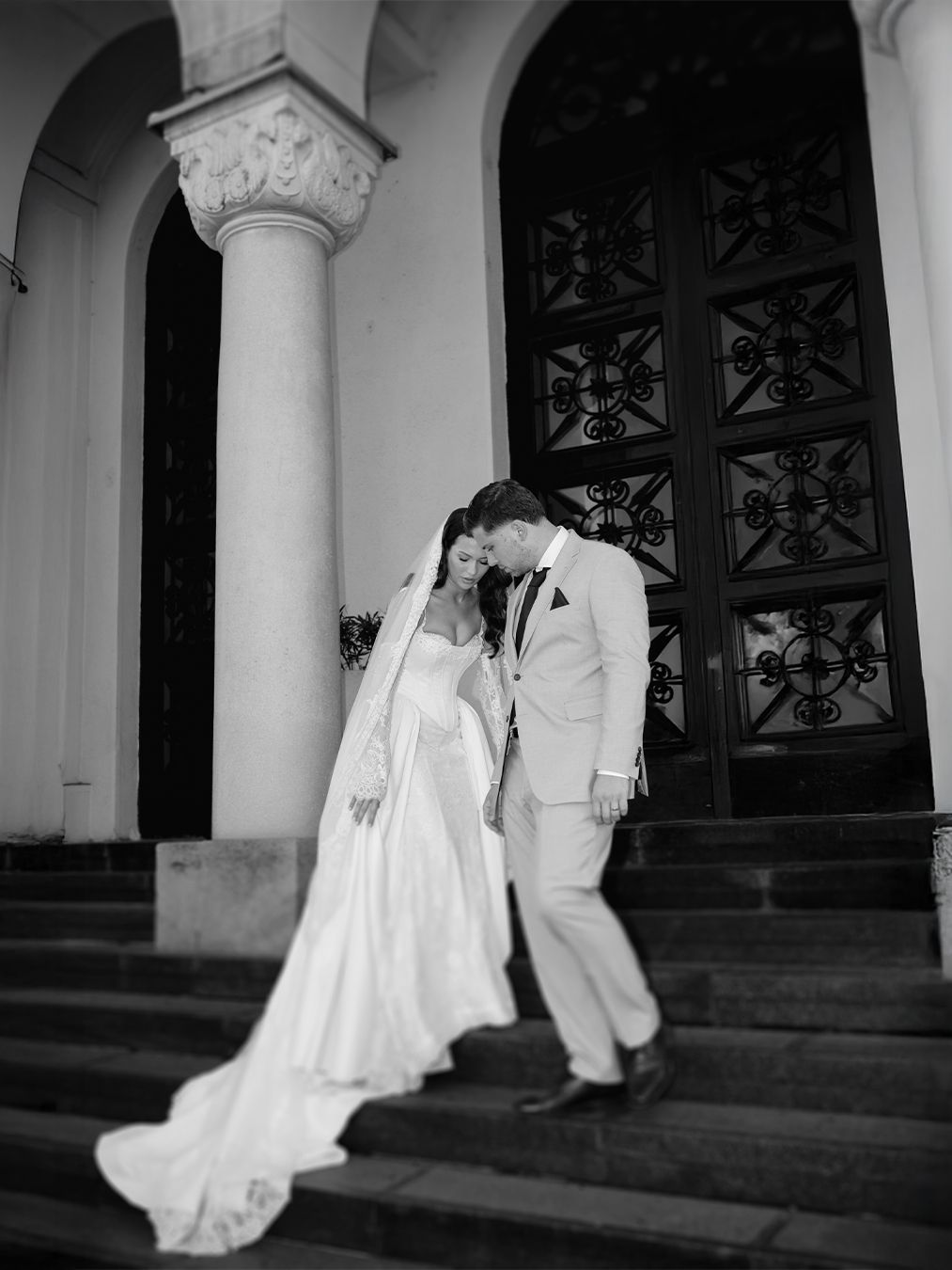 Black and white photo of bride and groom descending church steps, bride in flowing gown with veil.