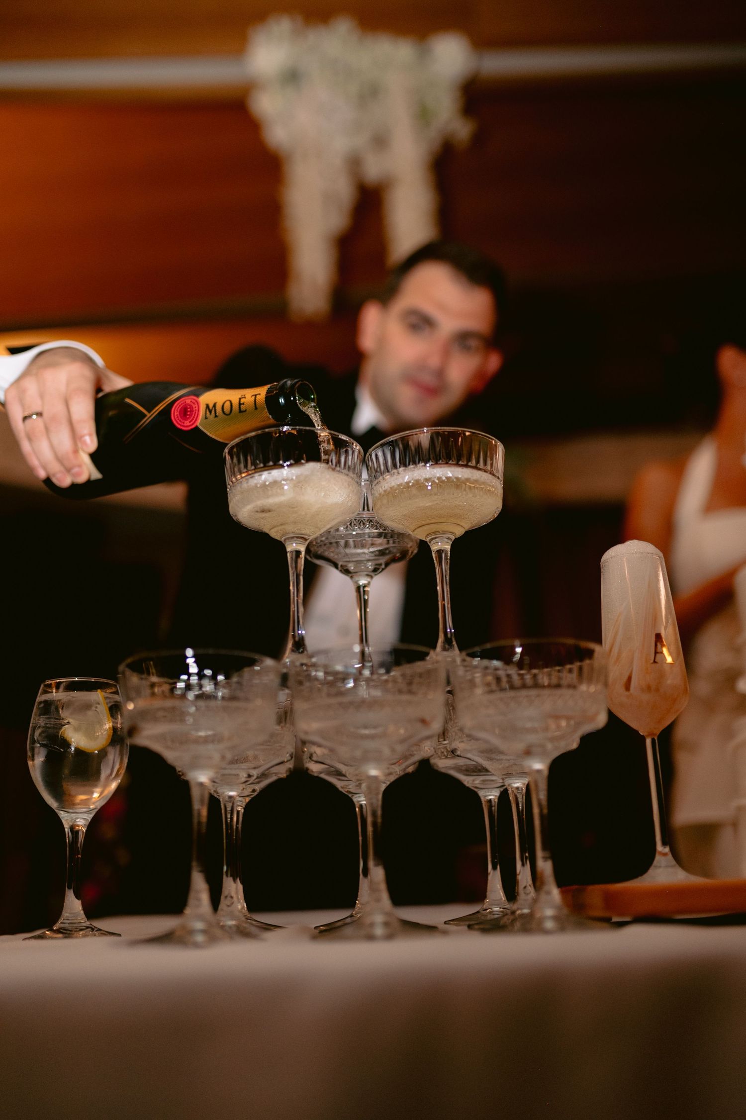 Man pouring Moet champagne into a pyramid of coupe glasses at an elegant wedding reception celebration.