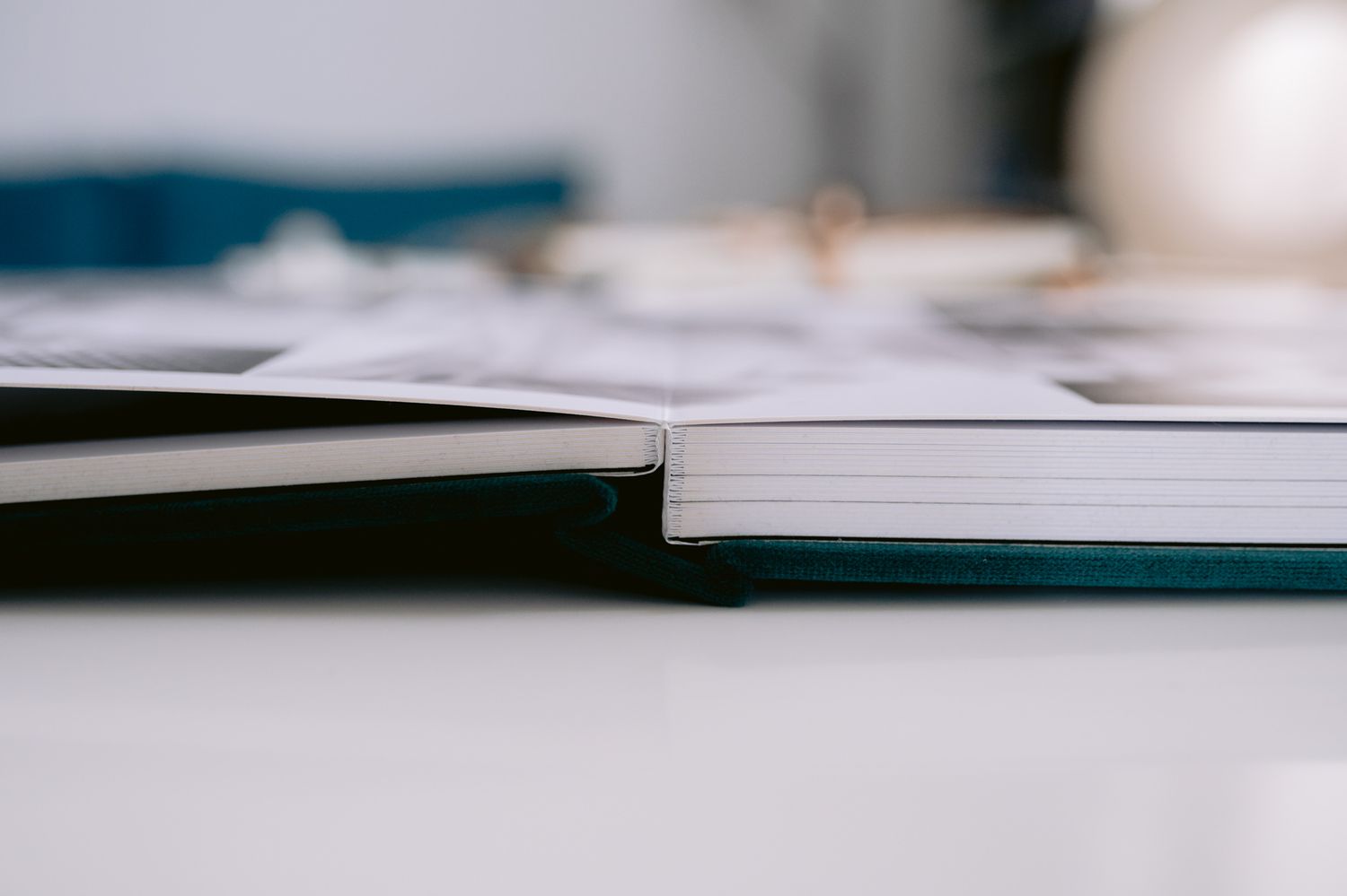Close-up of an open hardcover photo book with teal spine resting on a white table.