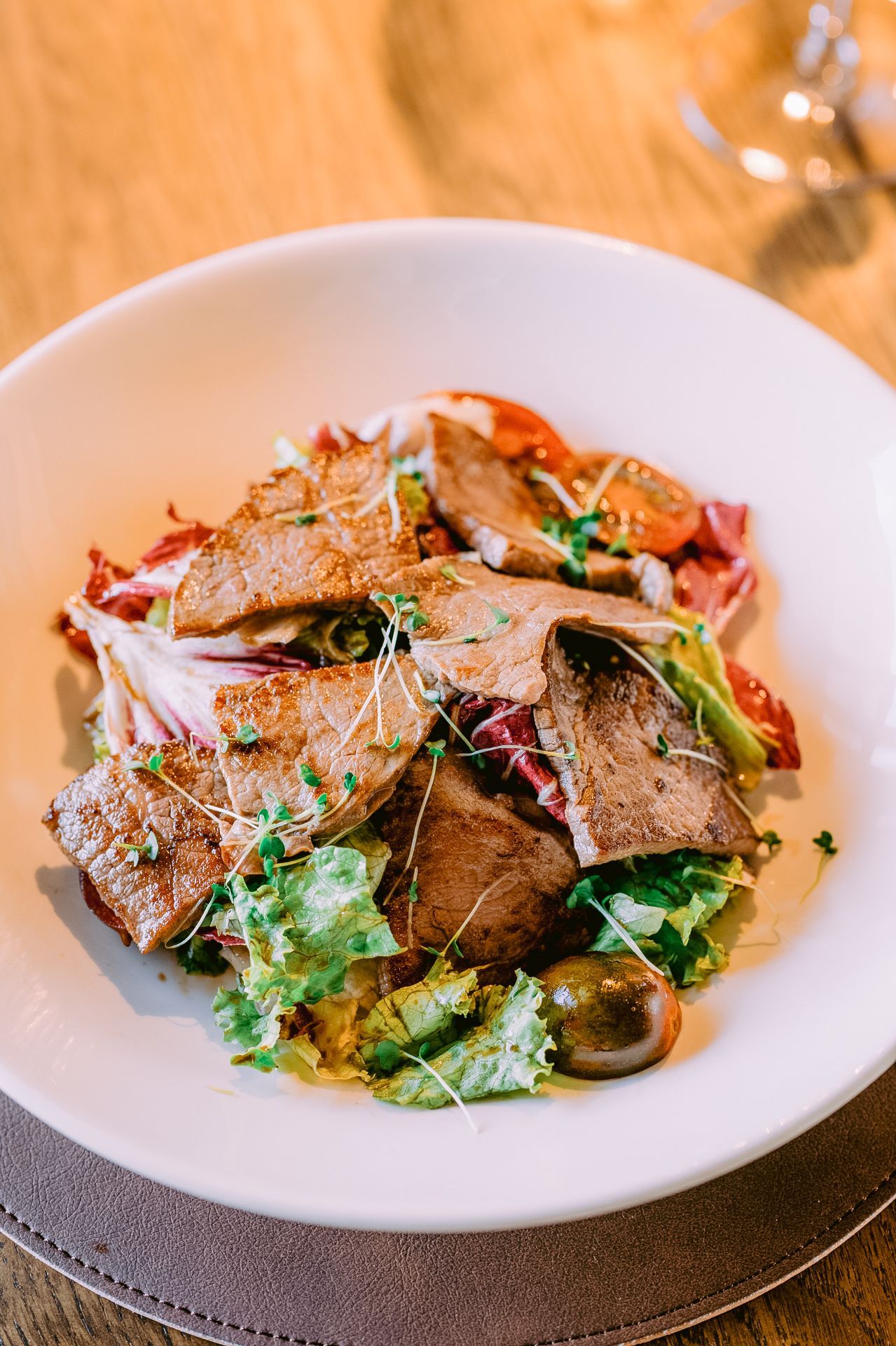 Beautifully plated meat dish with microgreens and garnishes on a white plate.