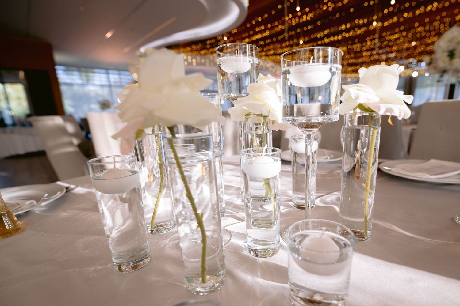 Modern wedding reception table setup with glowing string lights and glassware.