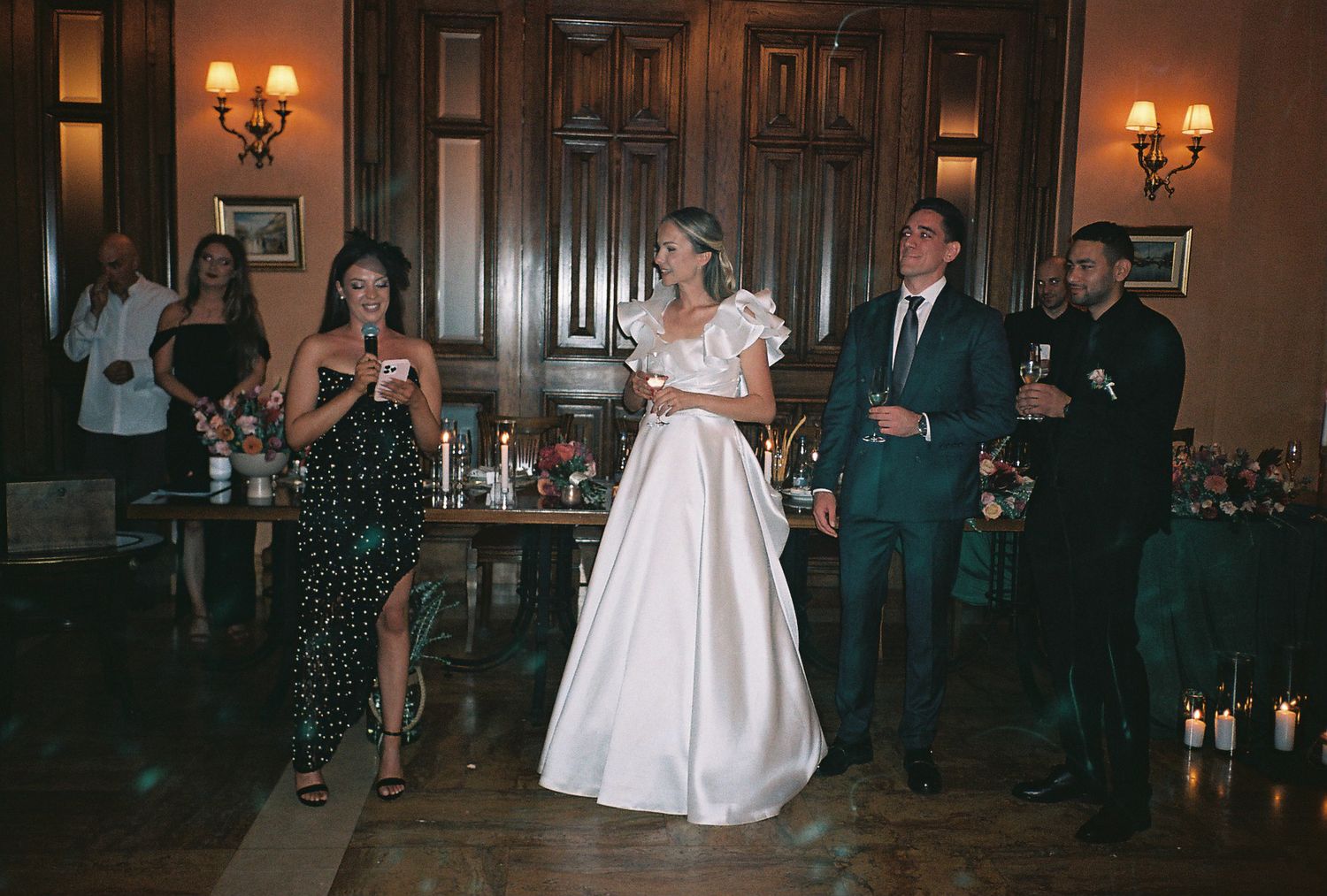 A couple shares their first dance in a warmly lit ballroom surrounded by wedding guests and elegant decor.
