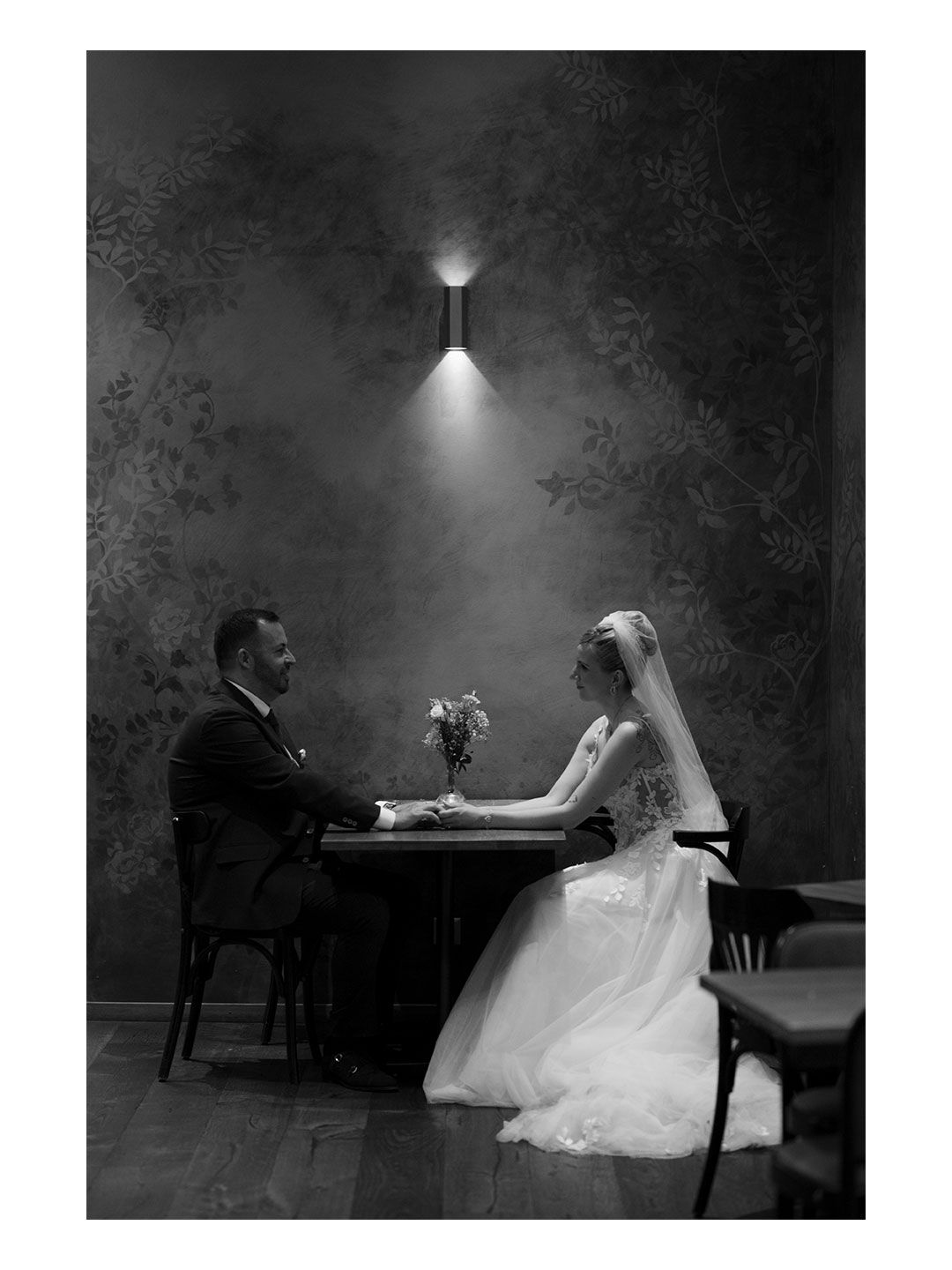 Crno-bijela fotografija mladenaca dok sjede za stolom ispod zidne lampe u elegantnom ambijentu Schaffhausen.