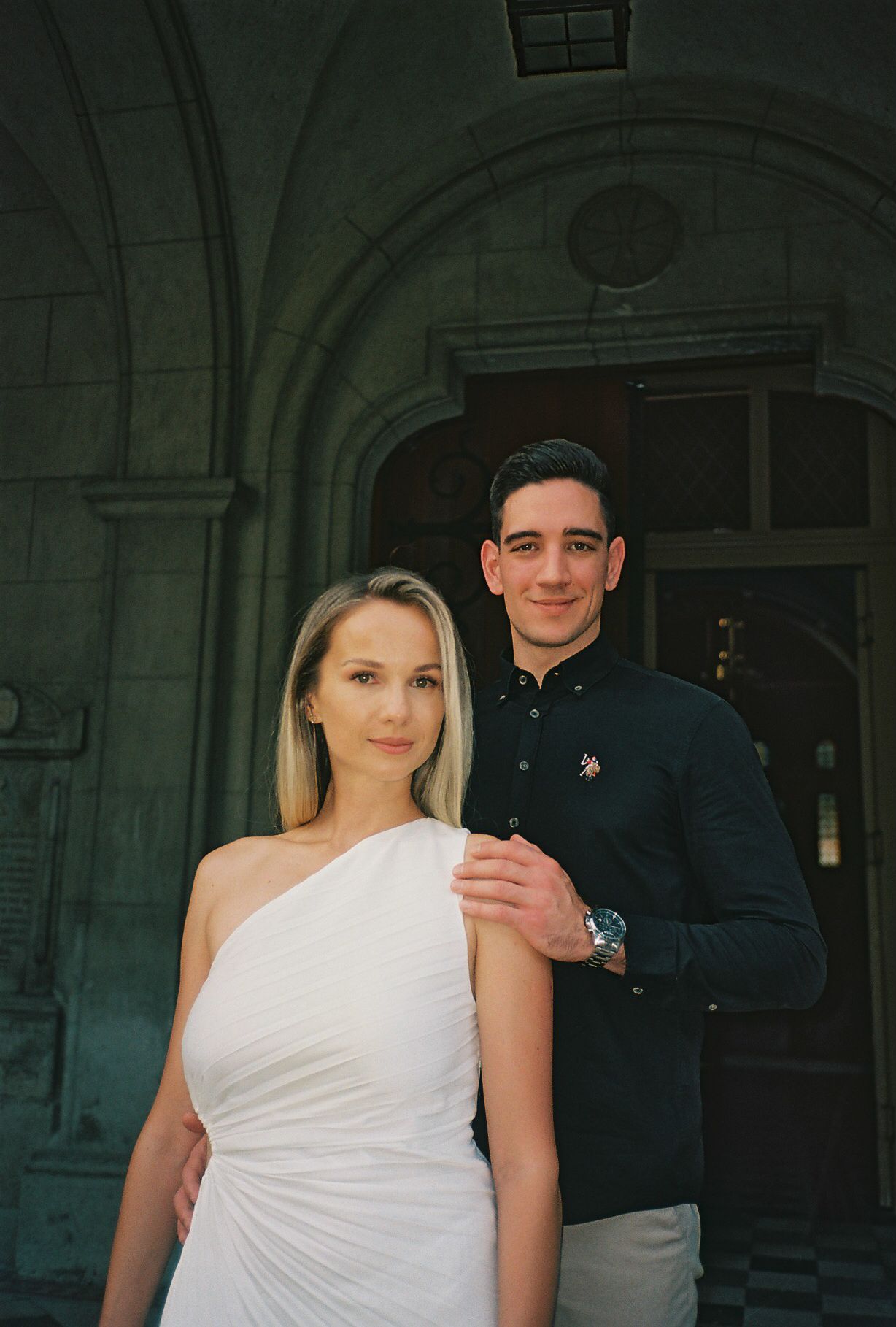A couple poses together in a series of four similar photos against a dark stone archway background.
