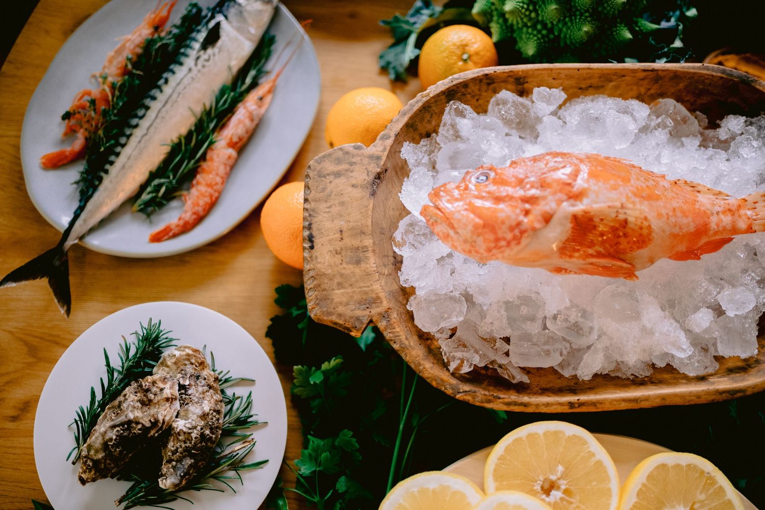 Fresh salmon on ice with mackerel, oyster, lemon slices, and herbs on a rustic wooden table.