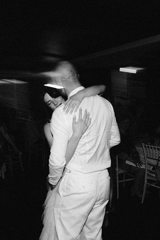 Black and white photo of a couple slow dancing and embracing at a wedding reception.