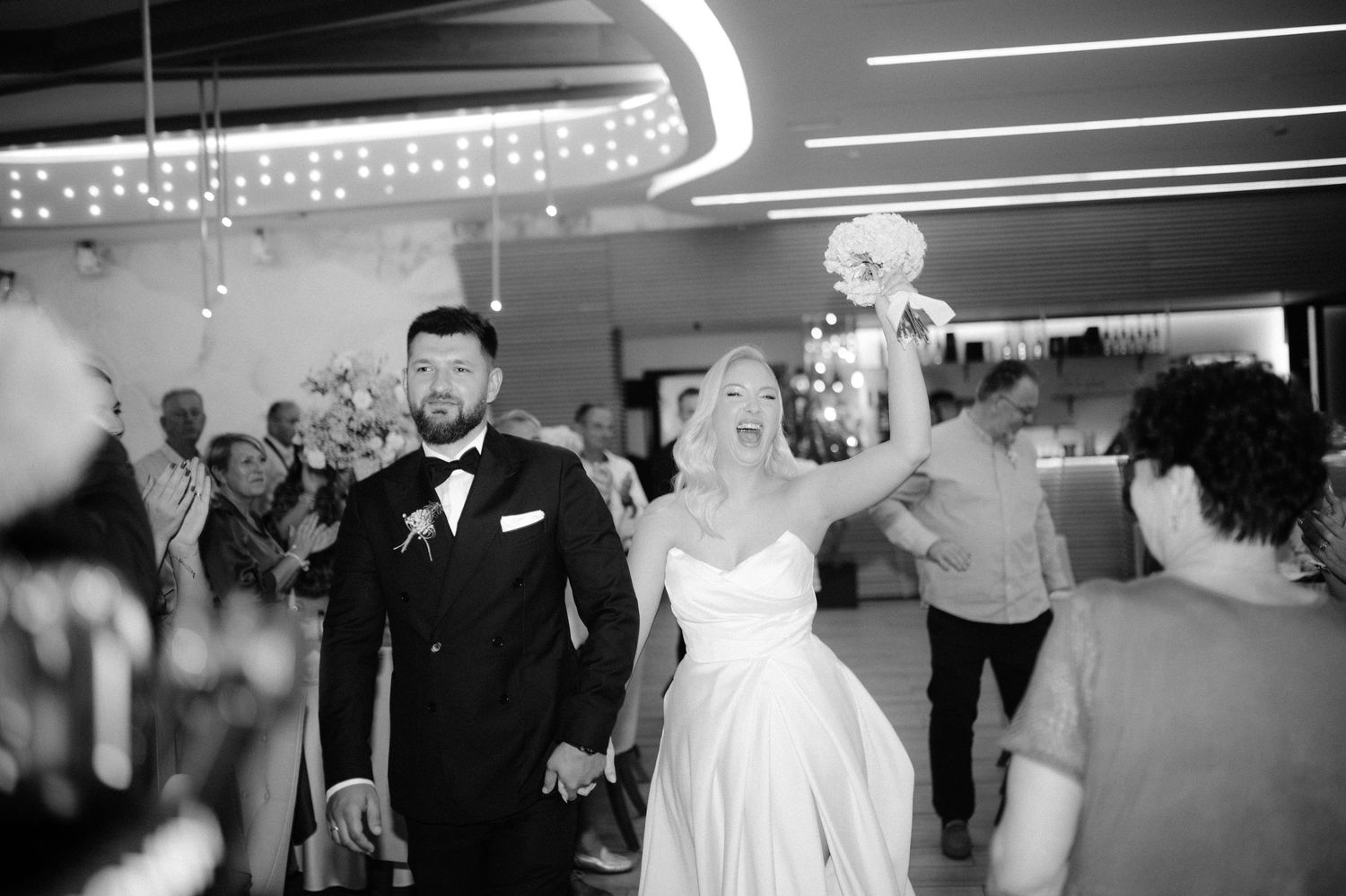 Black and white photo of a bride and groom holding hands making their grand entrance at their wedding reception.