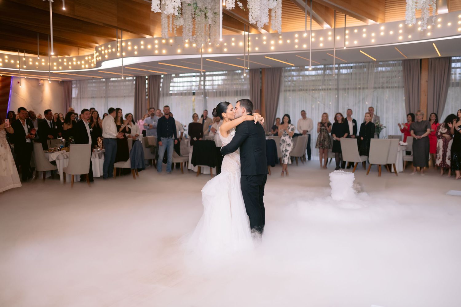 Bride and groom share first dance surrounded by dramatic dry ice fog on elegant wedding reception dance floor.