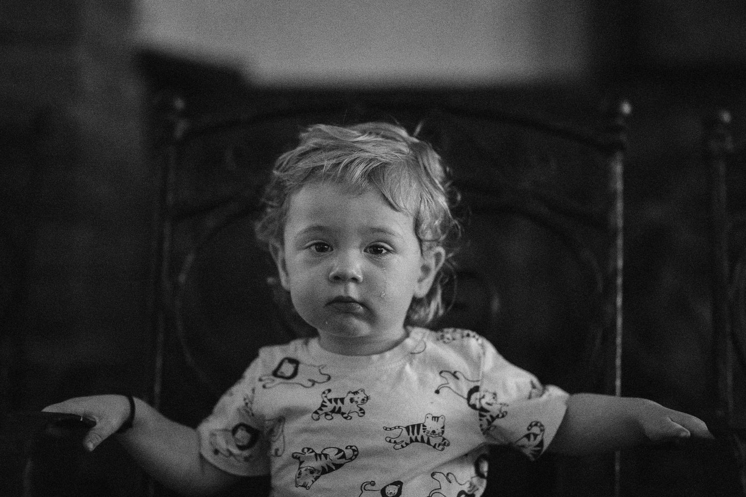 Black and white portrait of a curly-haired toddler sitting in a vintage chair with arms outstretched.