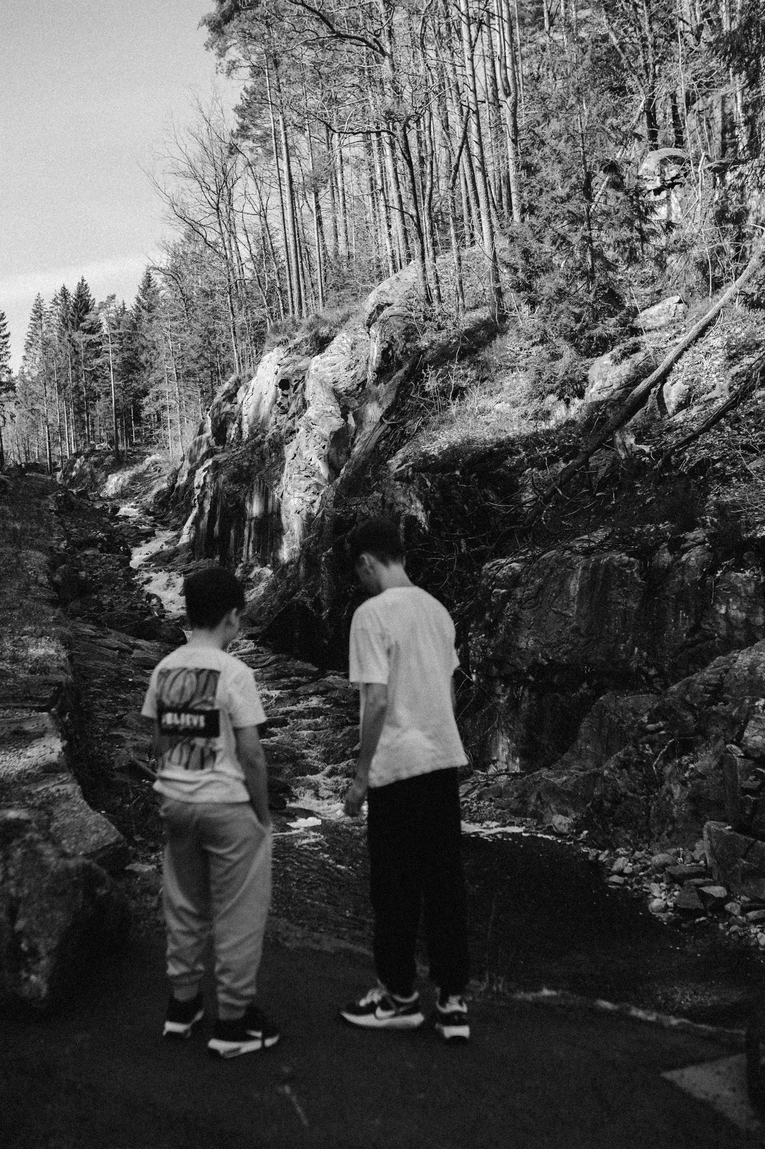 Visitors admire a scenic waterfall cascading down rocky cliffs in a forested area on a cloudy day.