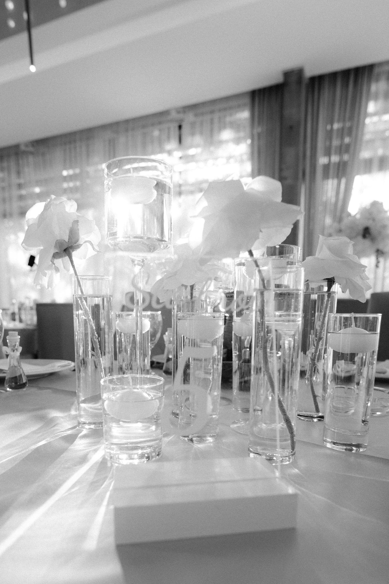 Black and white image of elegant table settings with glass vases and floral arrangements.