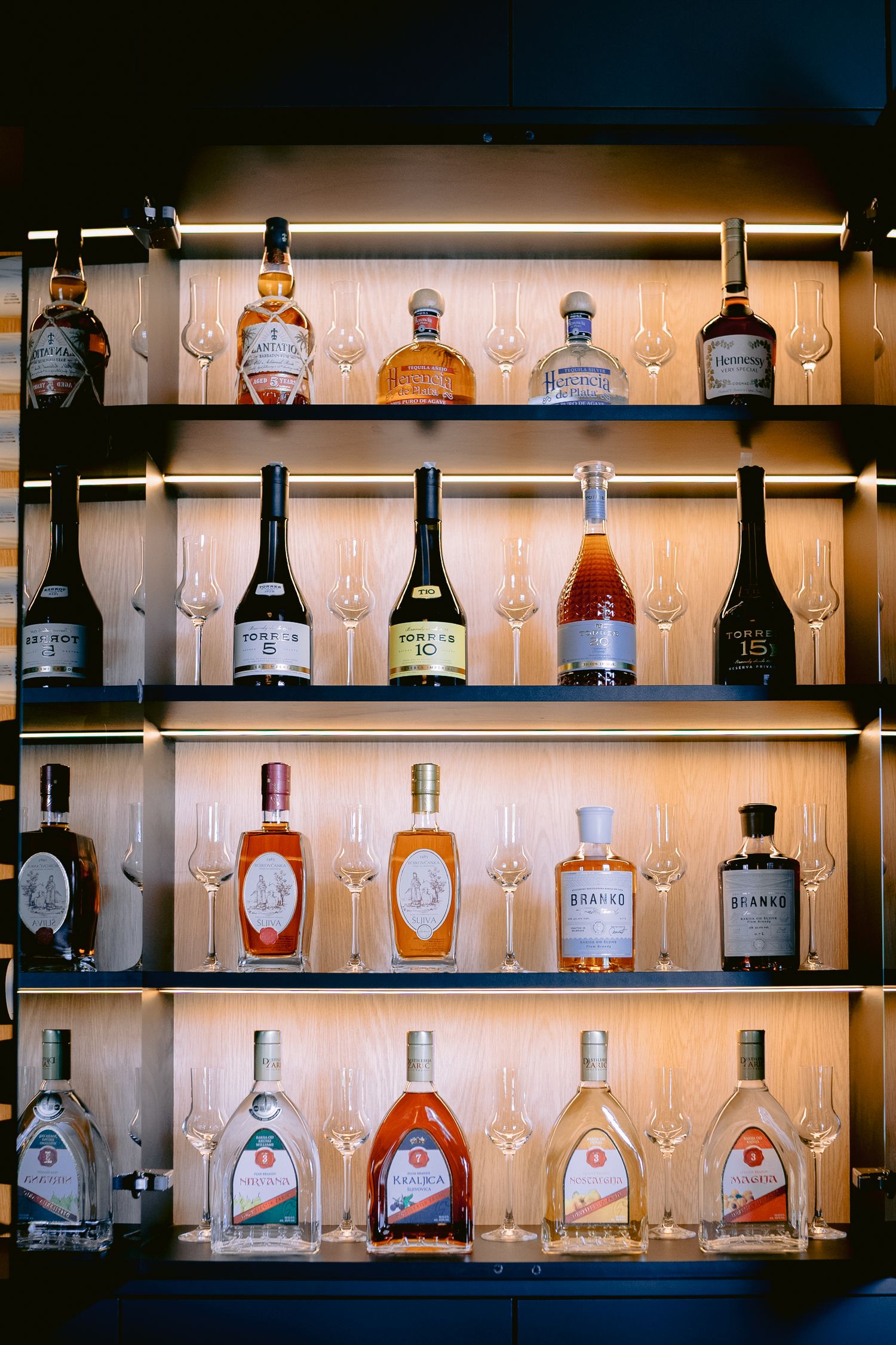 Illuminated bar shelf displaying various liquor bottles and cocktail glasses.