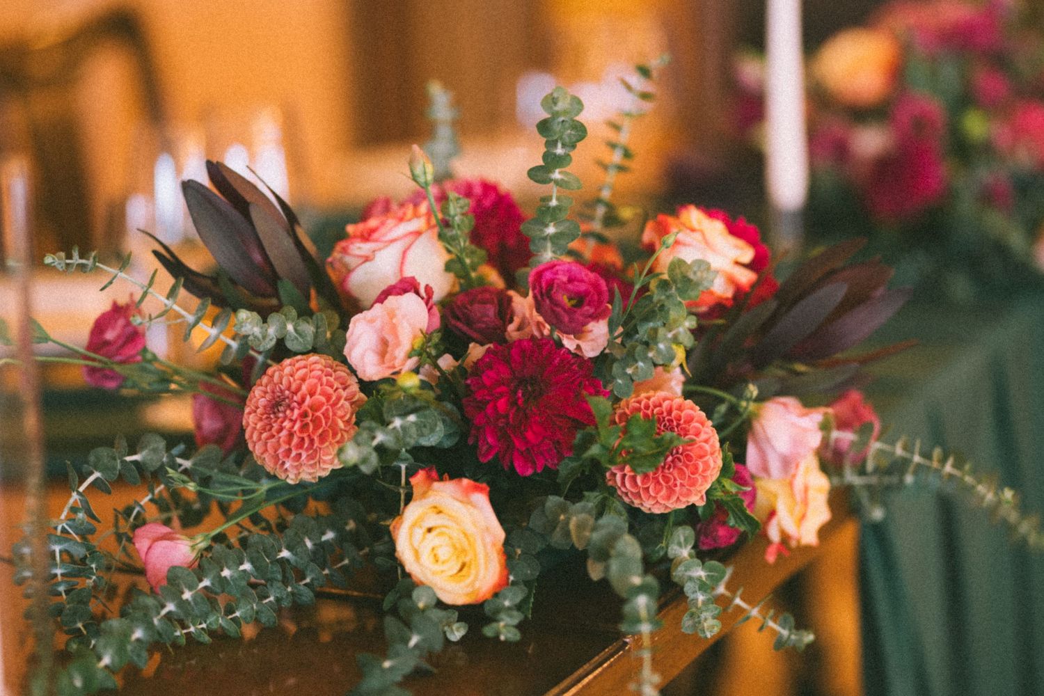 A vibrant floral arrangement with coral roses, peach blooms and eucalyptus greenery decorates a wooden surface.