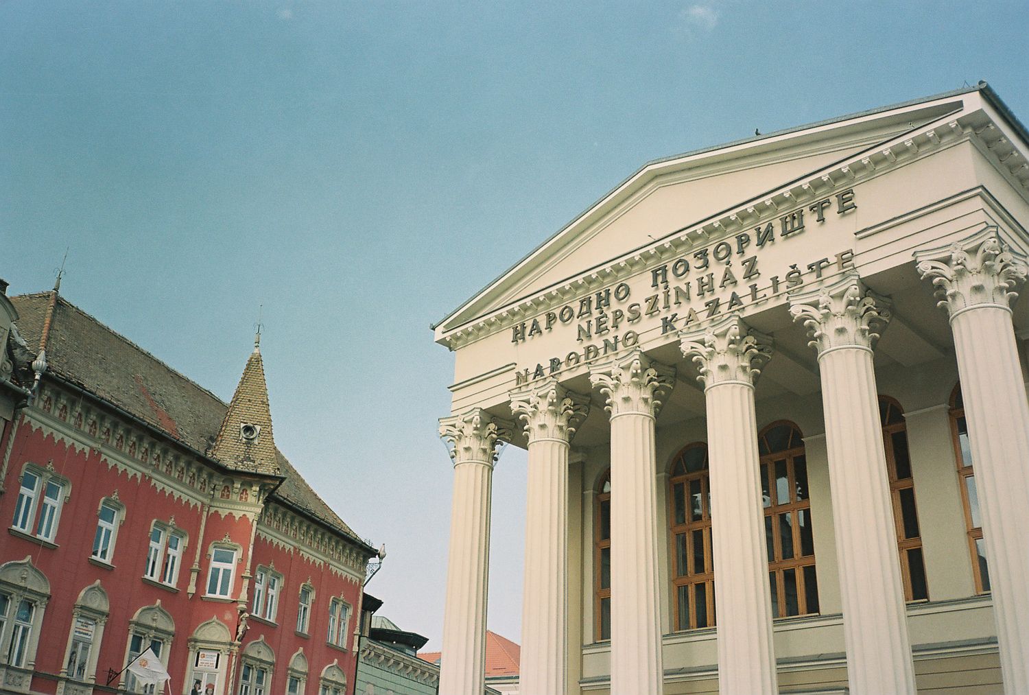 Historic buildings with neoclassical architecture and red brick facades line a city street under a bright blue sky.