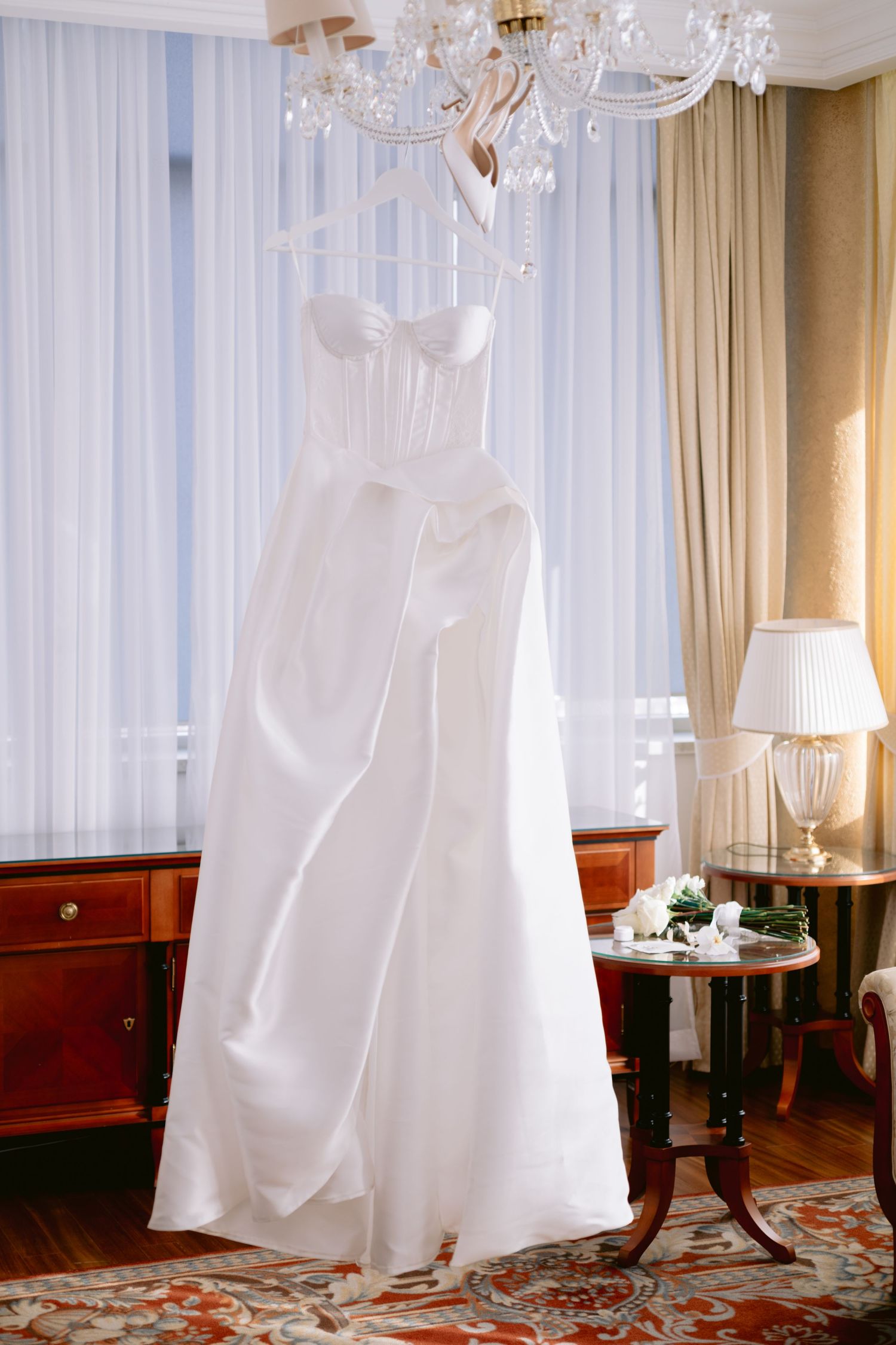 White wedding dresses hanging elegantly in a luxurious room with crystal chandeliers.