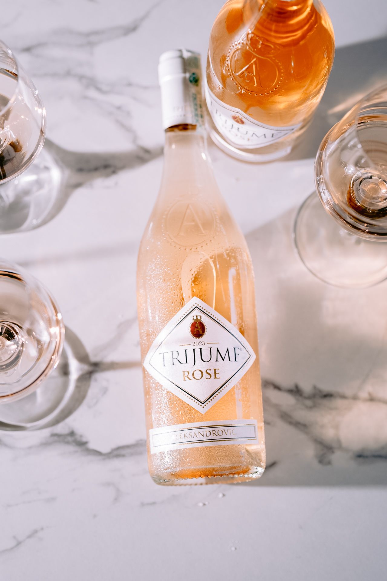 Close-up of Trijumi Rose wine bottle on white marble countertop with stemware.
