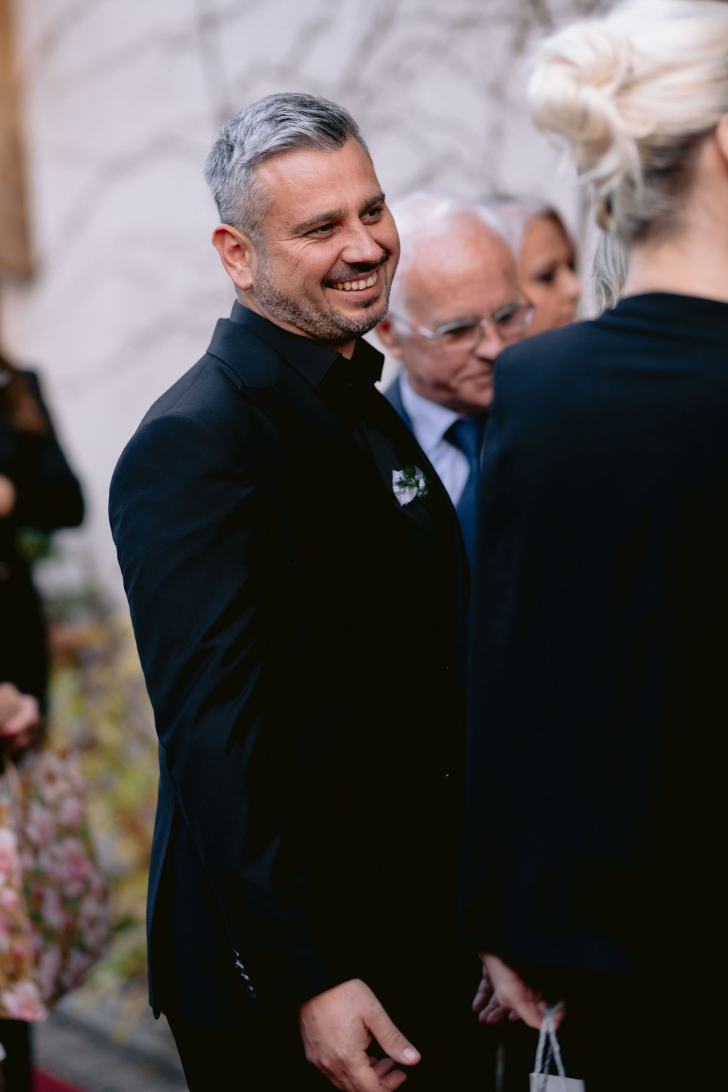 Group of people in formal attire laughing and smiling at an outdoor gathering.