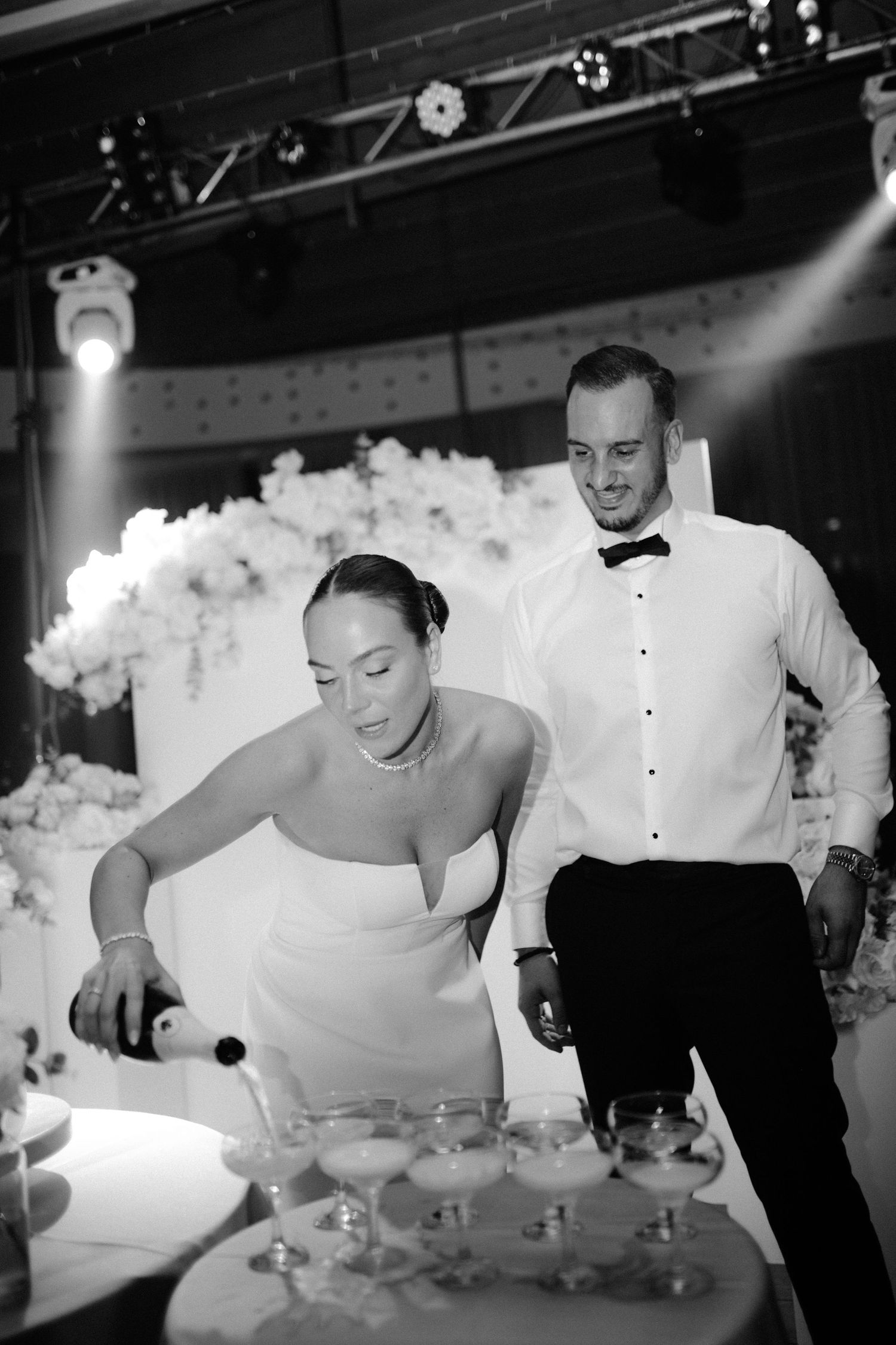 A couple at their wedding reception pouring champagne into a tower of glasses during the celebration.