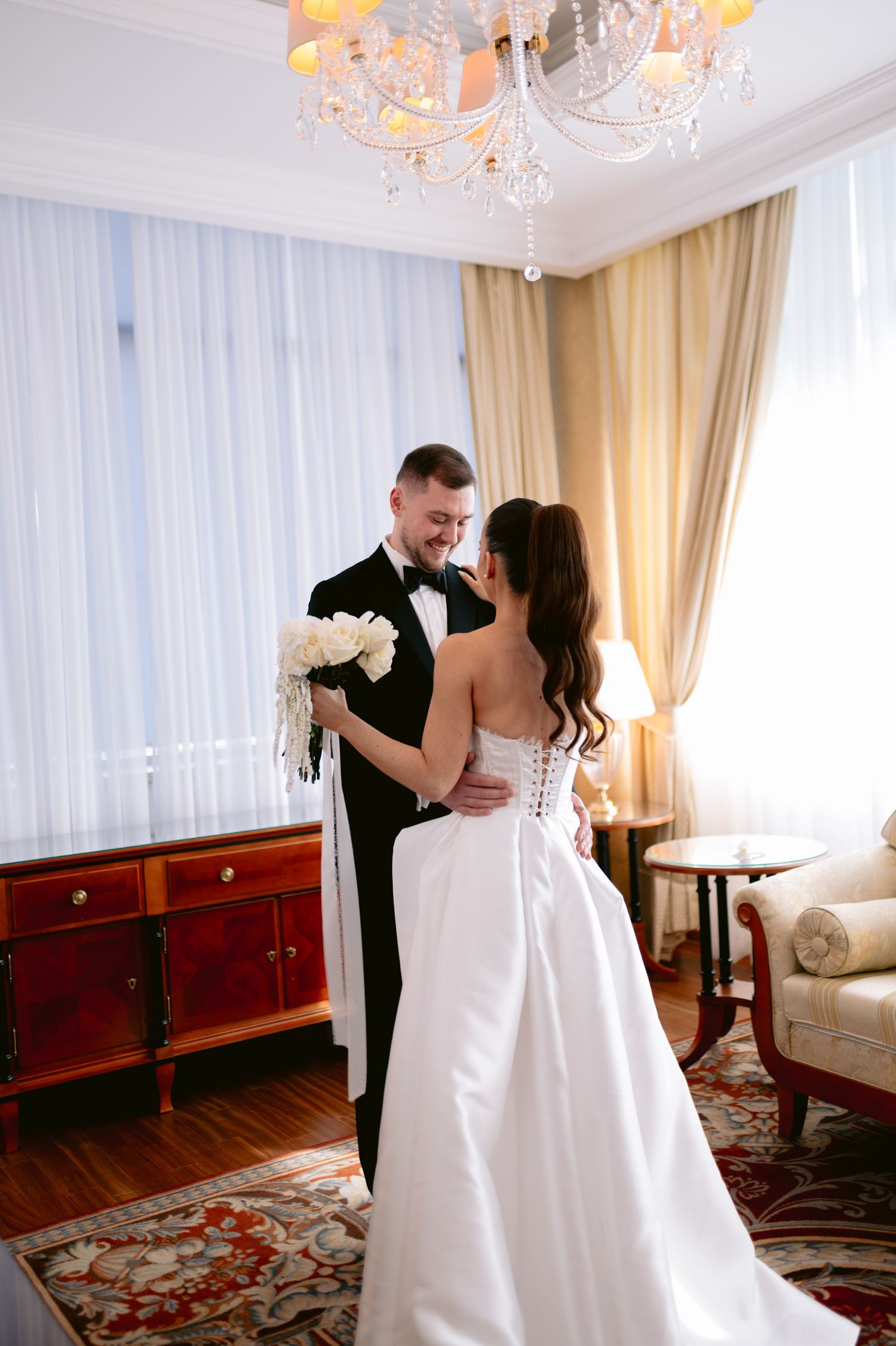 A couple shares a romantic moment in an elegant room with a crystal chandelier and ornate furnishings.