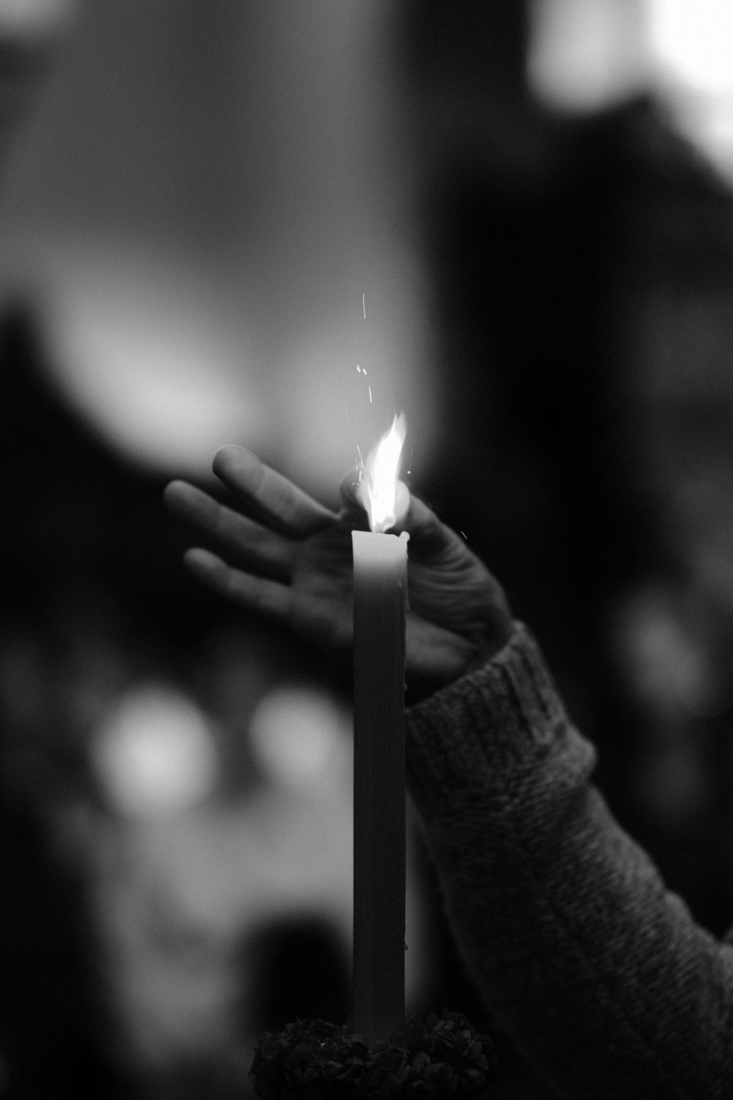 A hand wearing a dark knit glove holds a glowing white candle in a dimly lit setting.