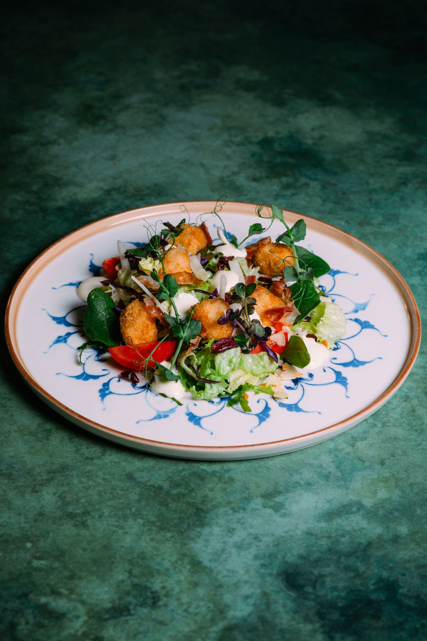 Elegant plated salad with colorful ingredients and garnishes served on a decorative white plate with blue accents.