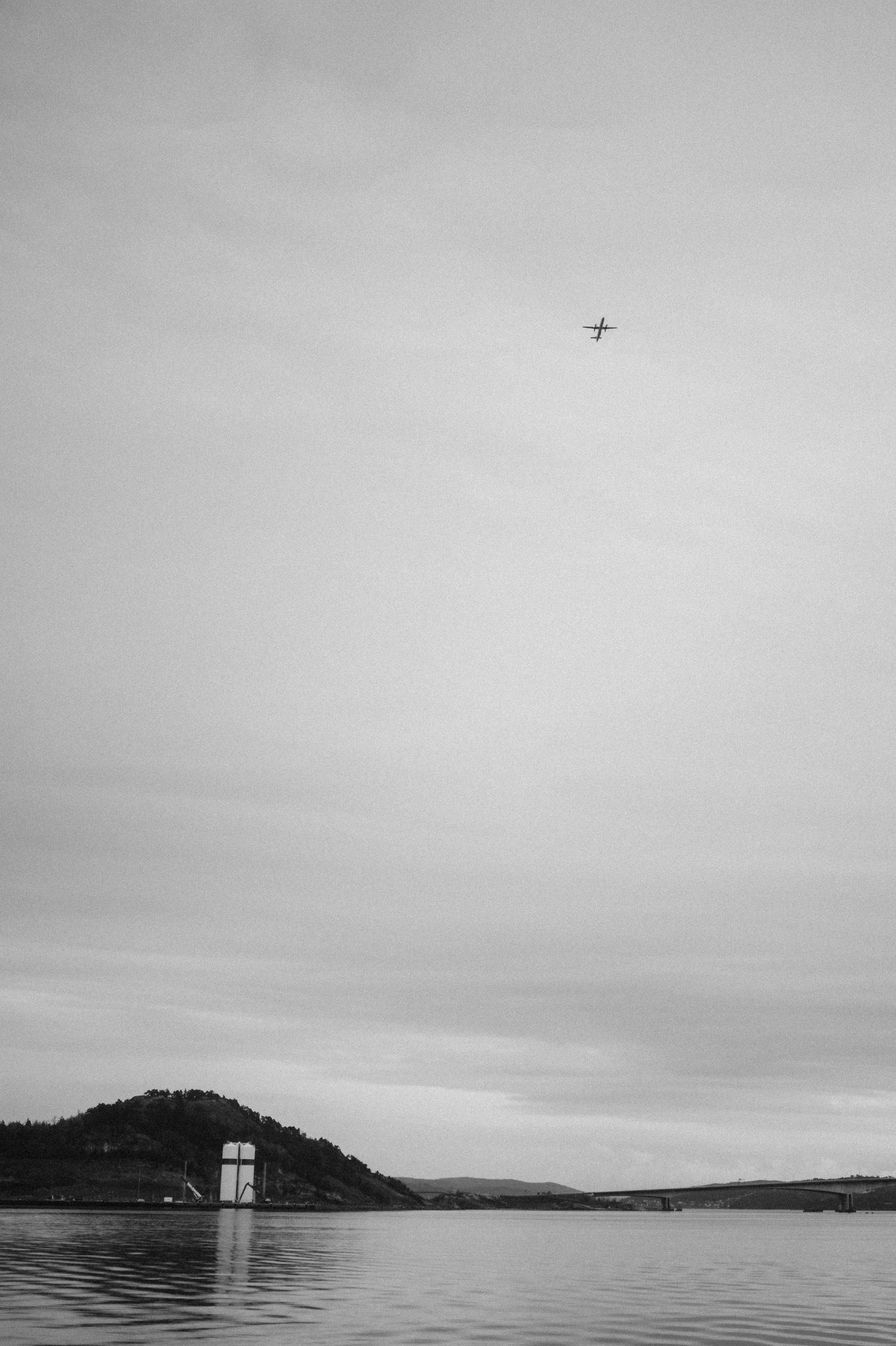 A serene black and white panoramic seascape with distant hills and calm waters stretching to the horizon.