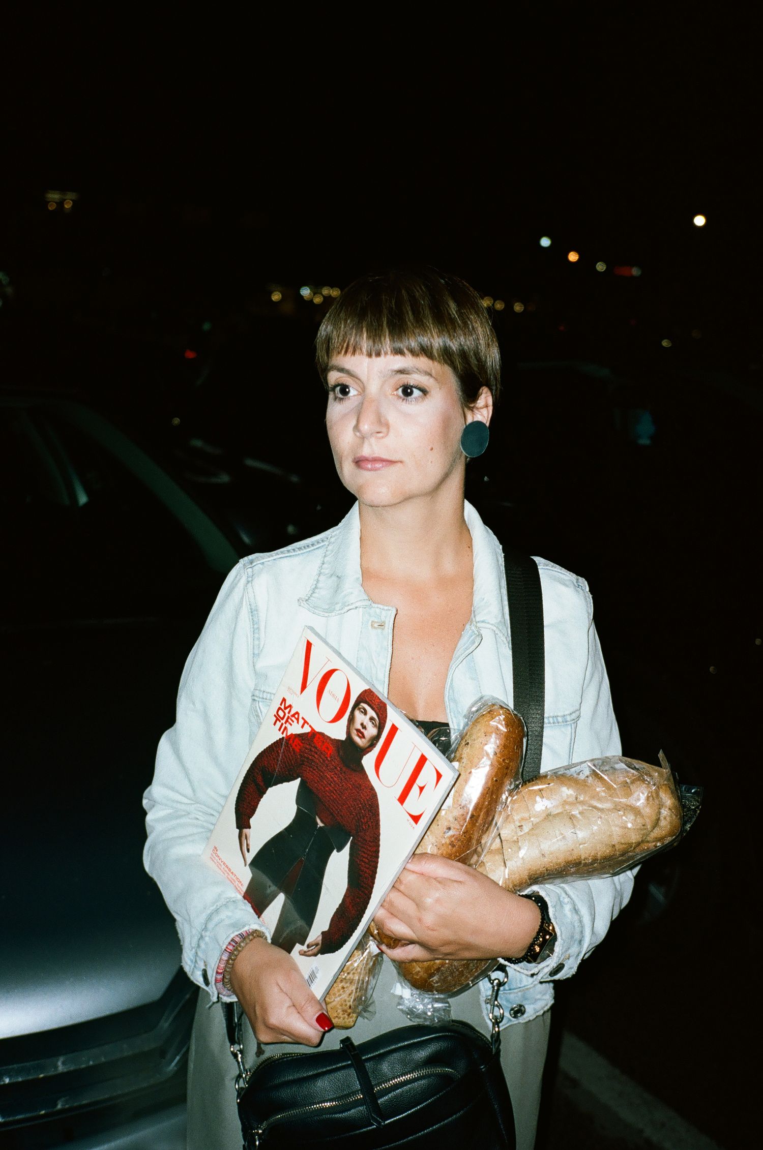 A person in a white shirt holds various items including shoes and shopping bags in a dark parking lot at night.