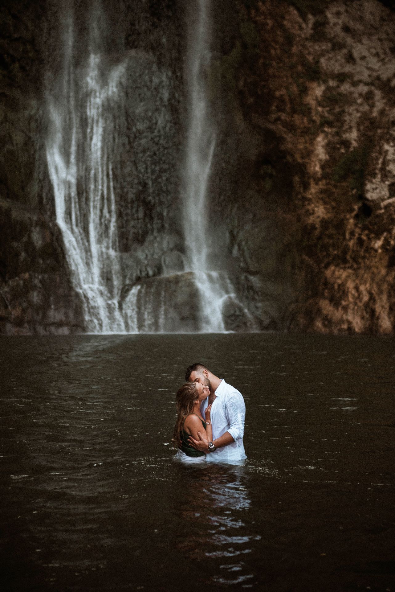 Couple sharing an intimate moment in a scenic waterfall pool.