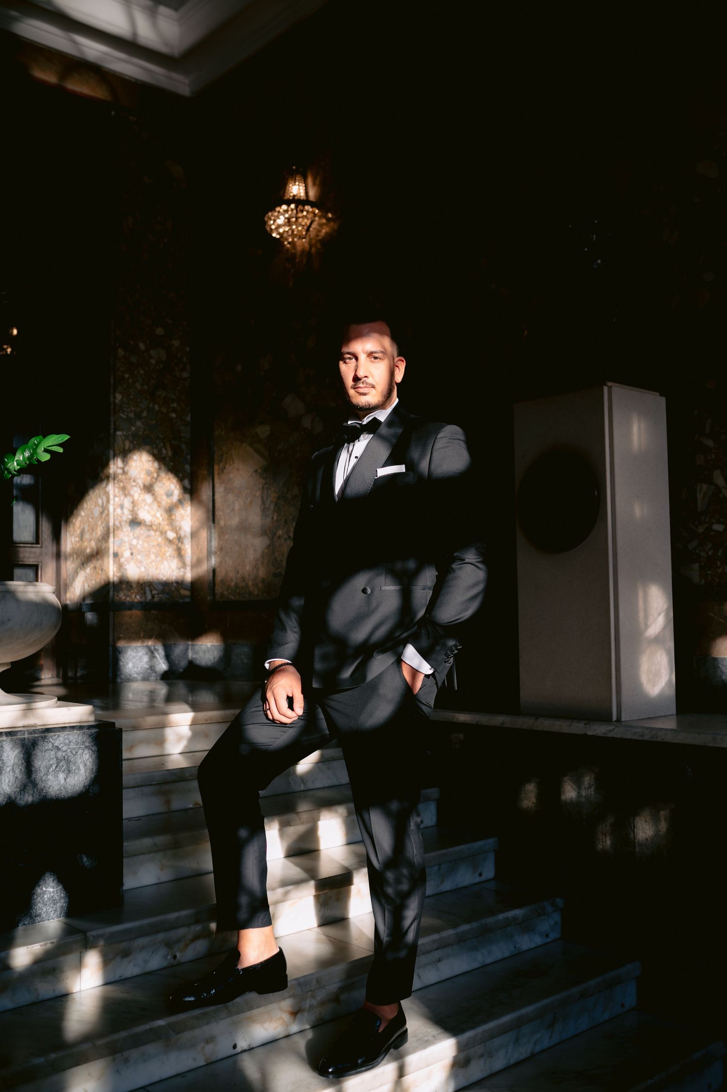 A person sits on dark wooden steps as dramatic shadows and light create a moody atmosphere.