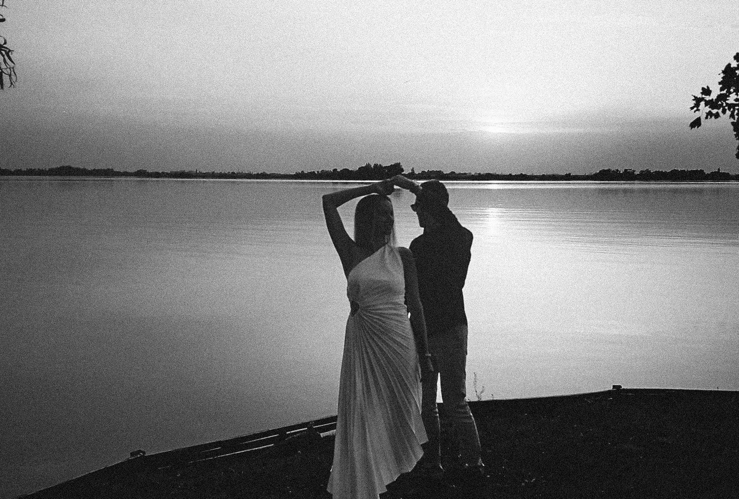 A series of black and white silhouettes show couples walking along a tranquil waterfront at sunset.