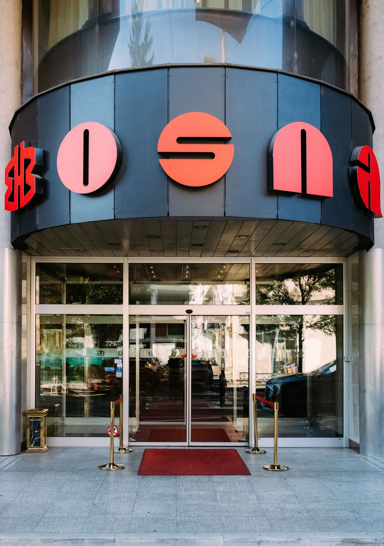 Modern building entrance with curved glass facade and red geometric signage mounted above glass doors.