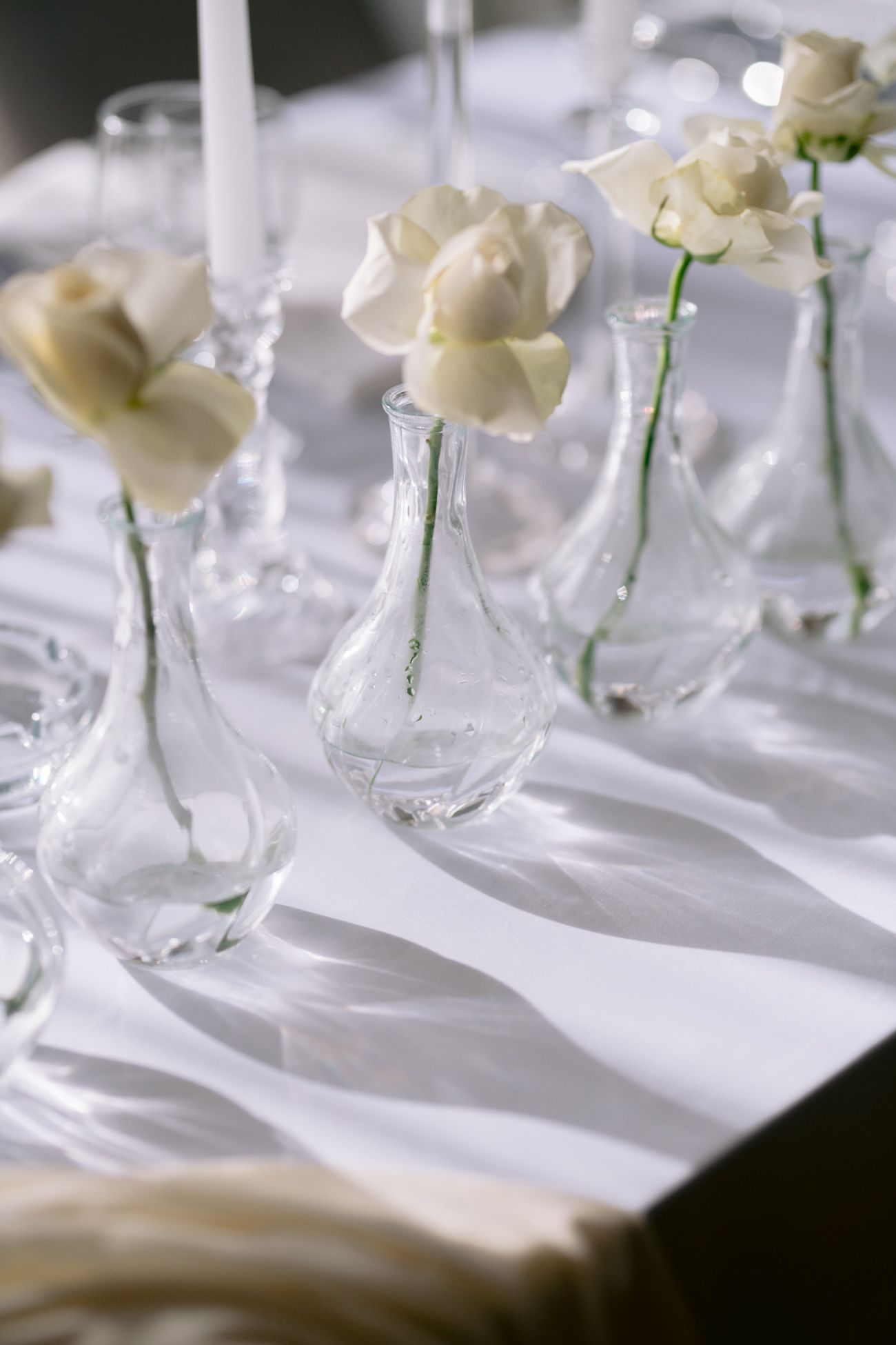 White roses in delicate glass bud vases on crisp white tablecloth.