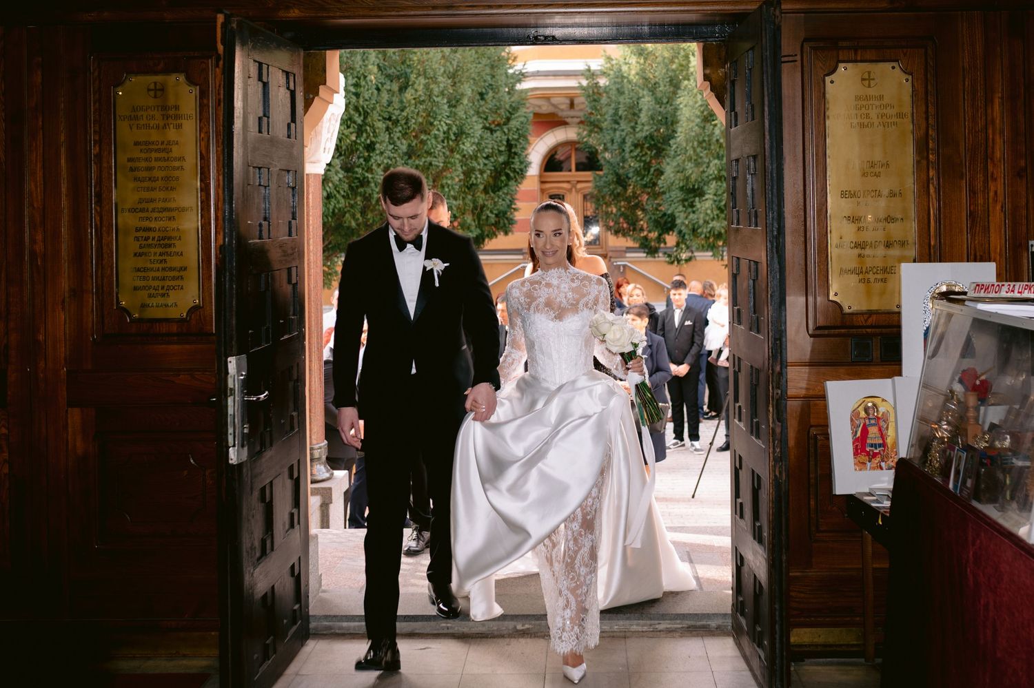 A wedding couple walks down a rustic wooden hallway while guests follow behind during a joyous celebration.