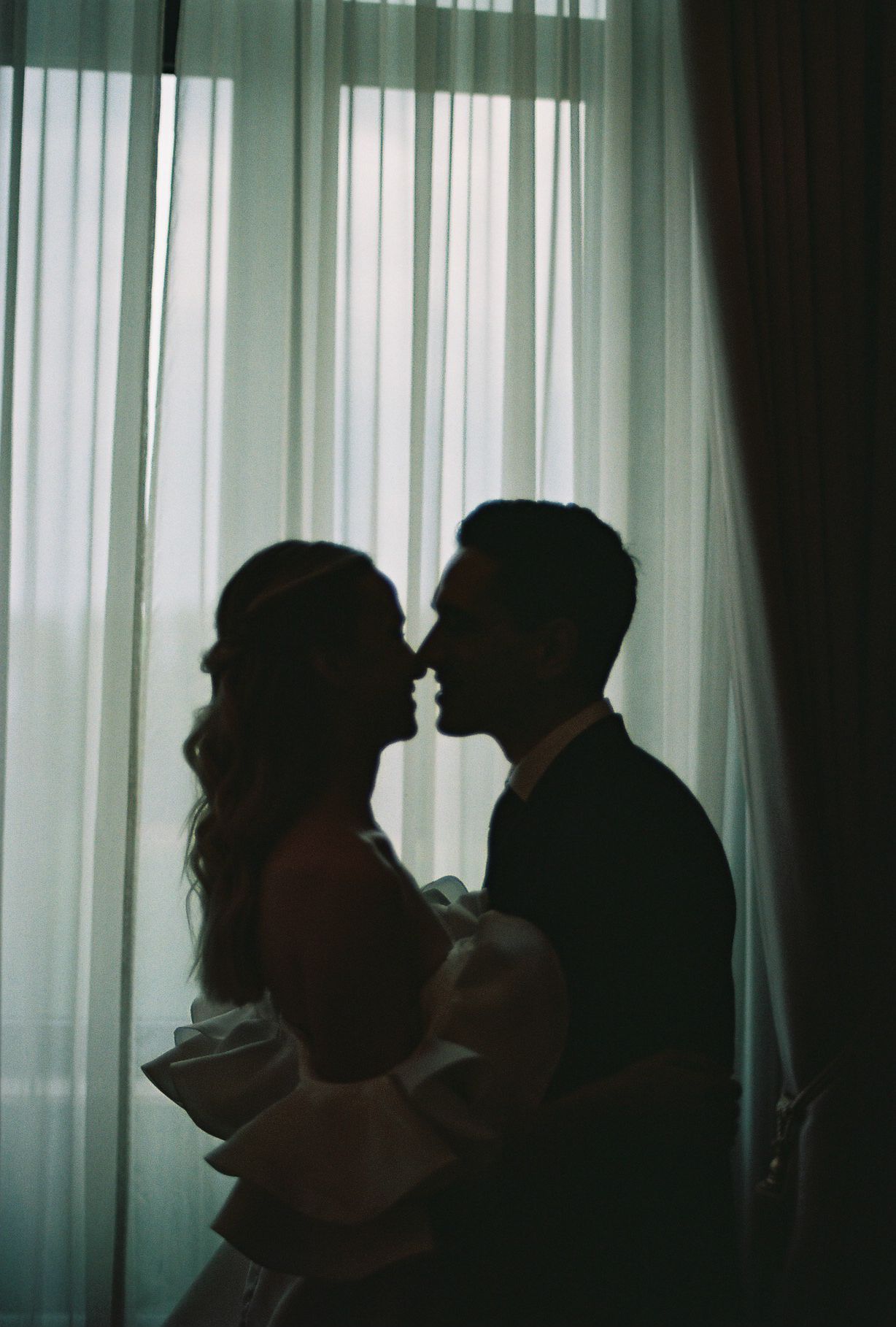Silhouettes of people standing against a bright window with sheer curtains creating a dramatic backlit effect.