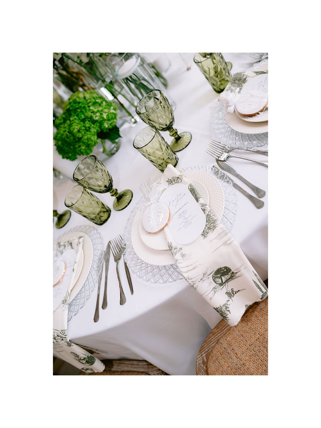 Elegant table setting with green goblets, white linens, silver cutlery, lace placemats, and fresh hydrangea centerpieces.