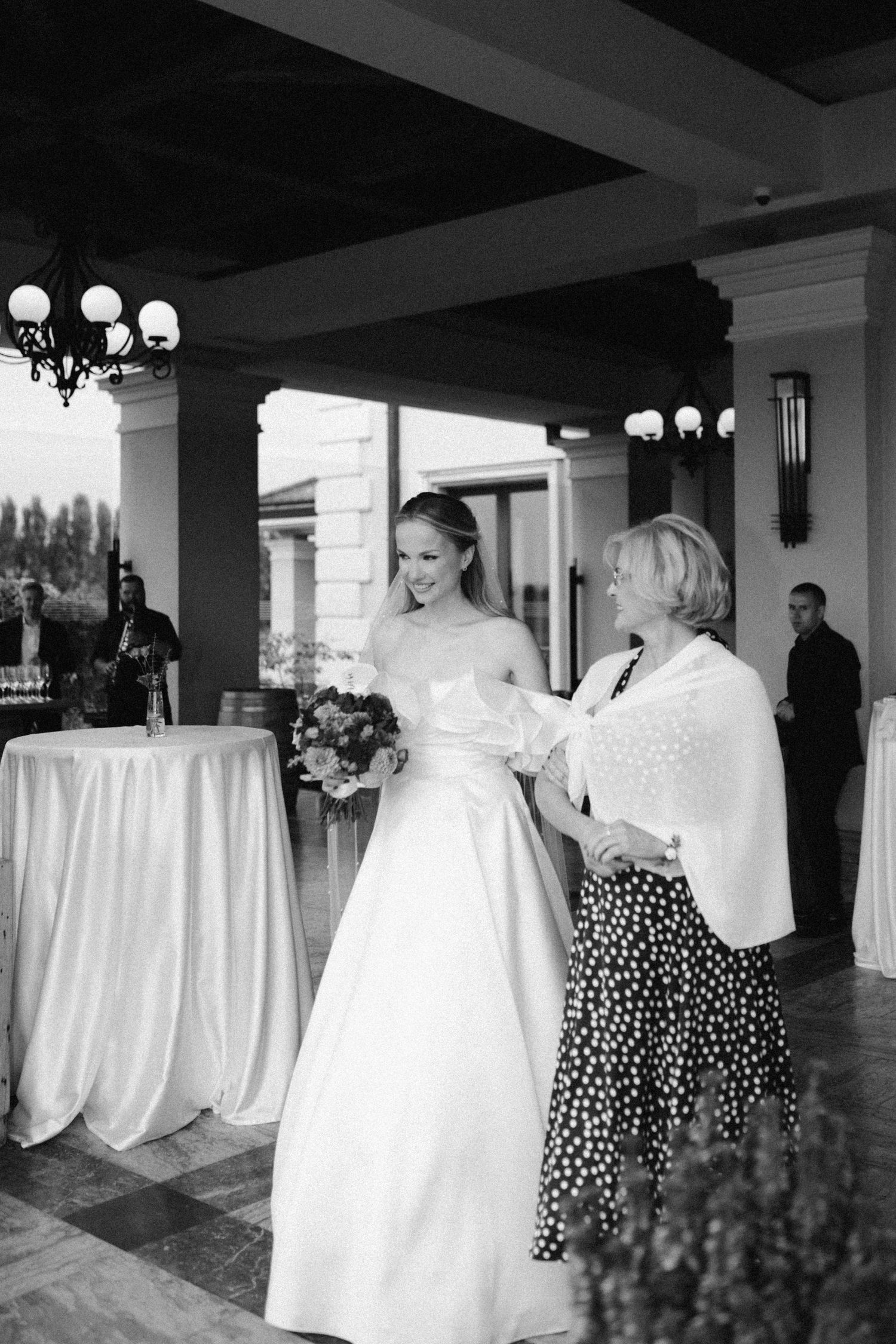 Elegant wedding reception scene with a bride in white gown and guest in polka dot skirt standing by decorated table.